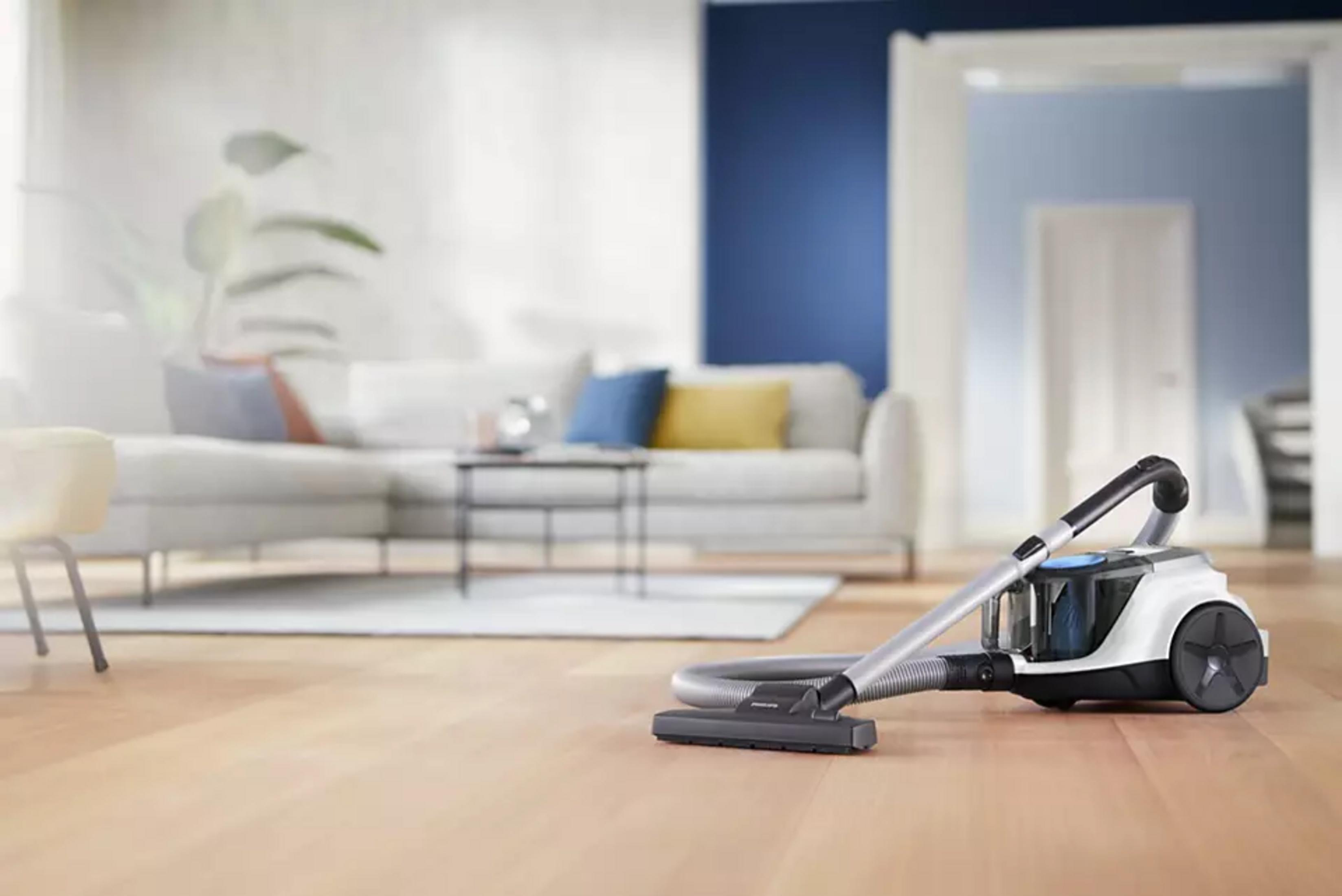 Ein moderner Staubsauger steht auf einem Holzboden vor einem Sofa.