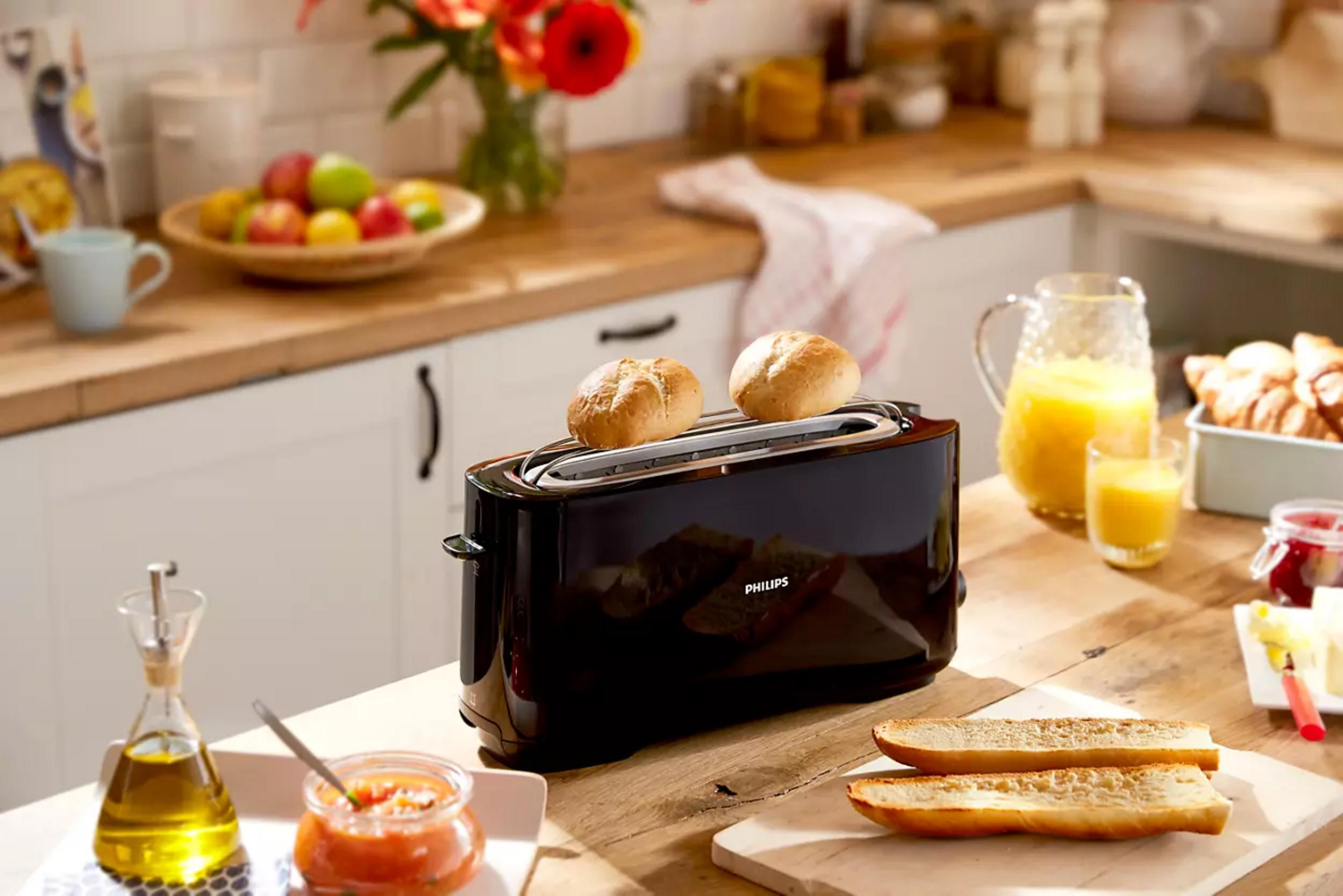 Un tostapane nero con due panini, succo e croissant nelle vicinanze.