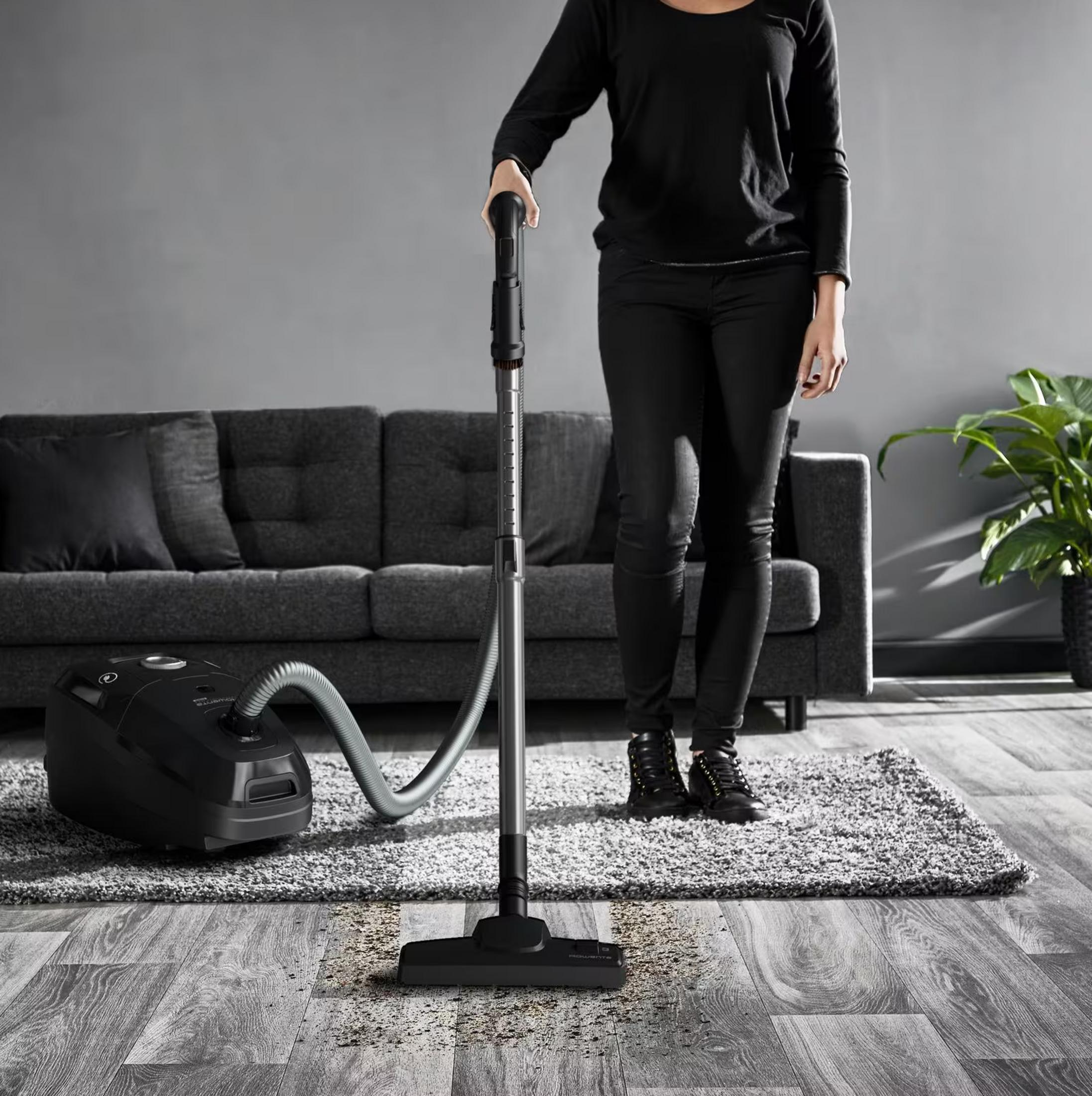 Osoba odkurza brudną drewnianą podłogę czarnym odkurzaczem.