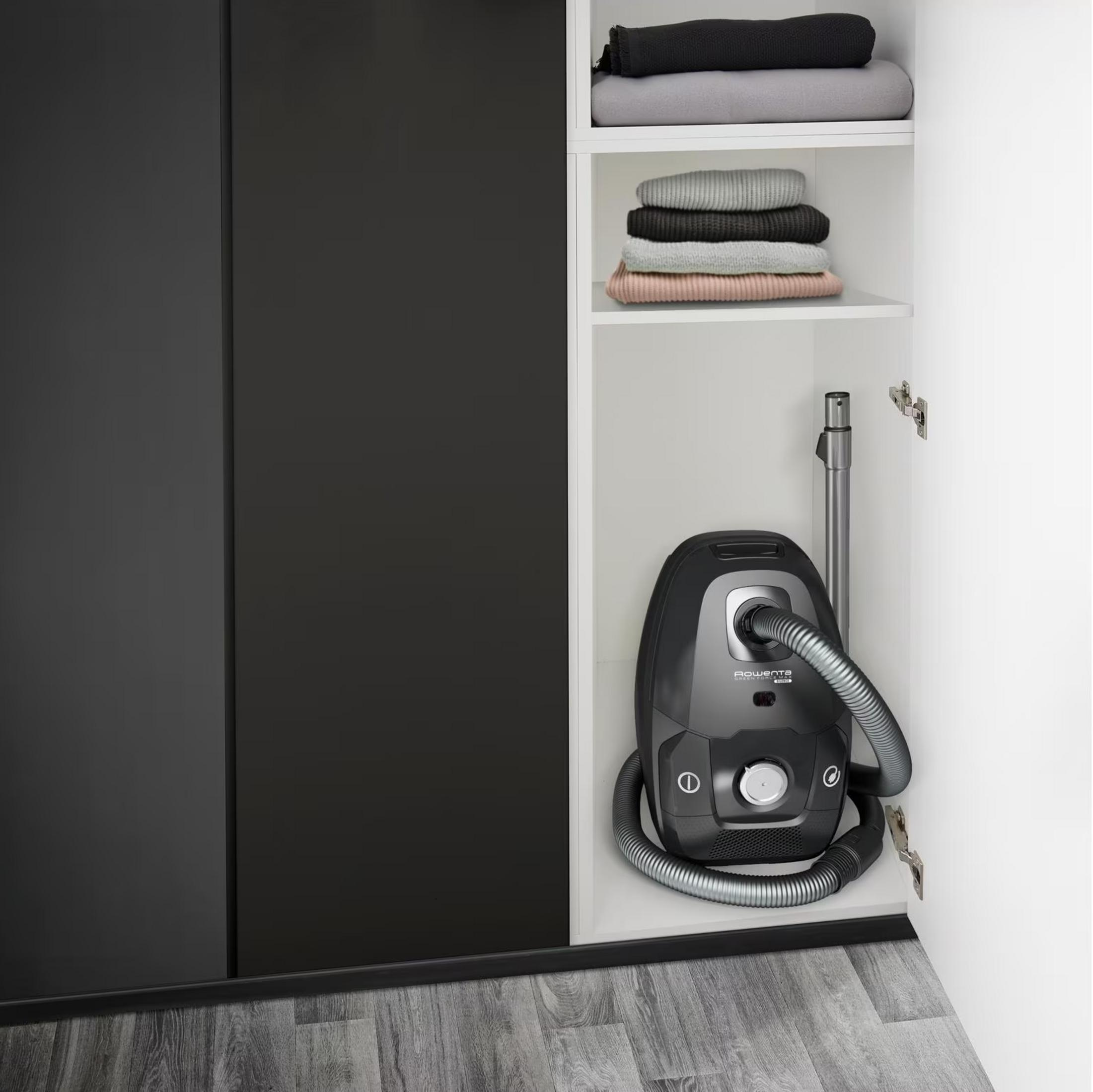 Ciemny odkurzacz z wężem stoi w otwartej szafie.