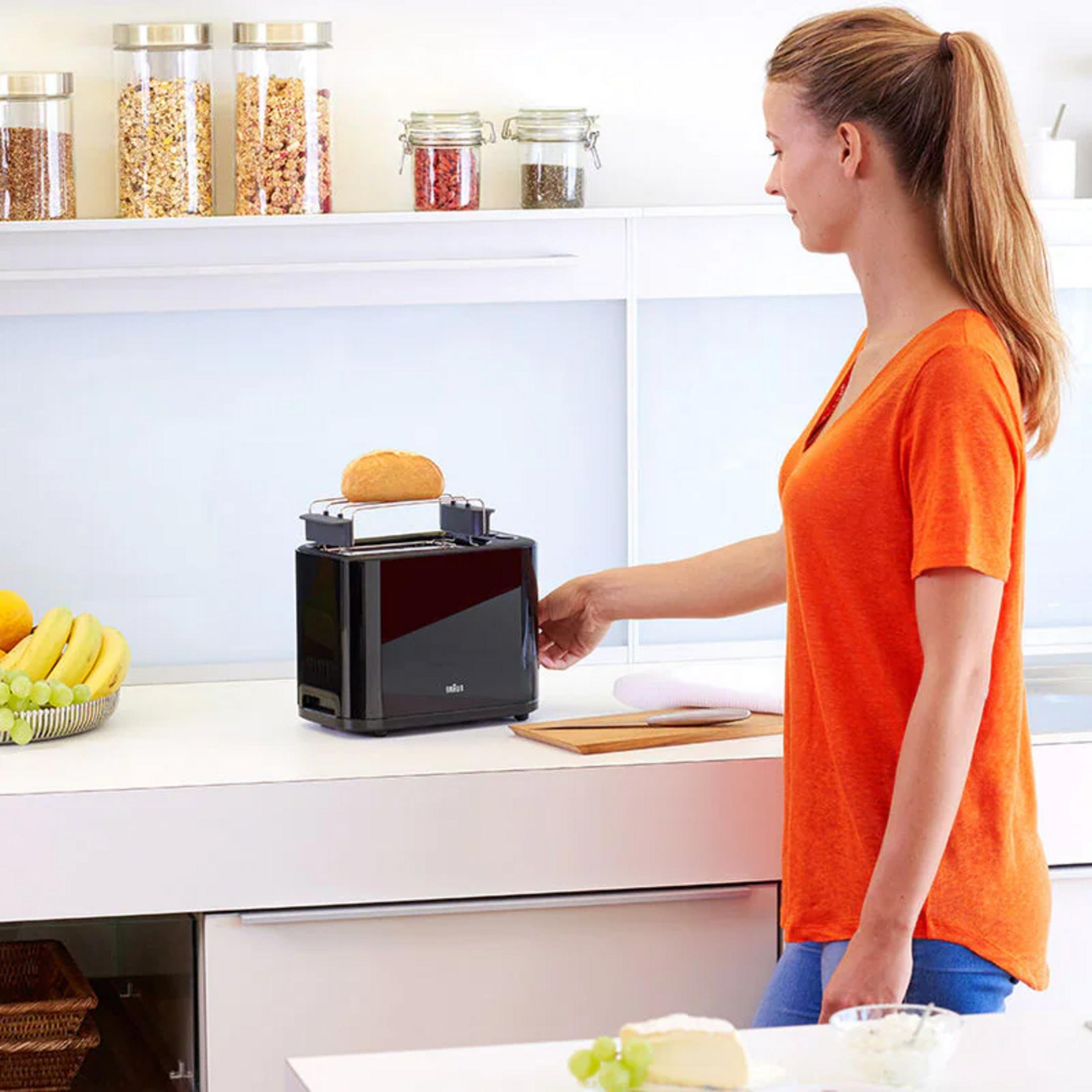 Una donna in maglia arancione usa un tostapane con un panino dentro.