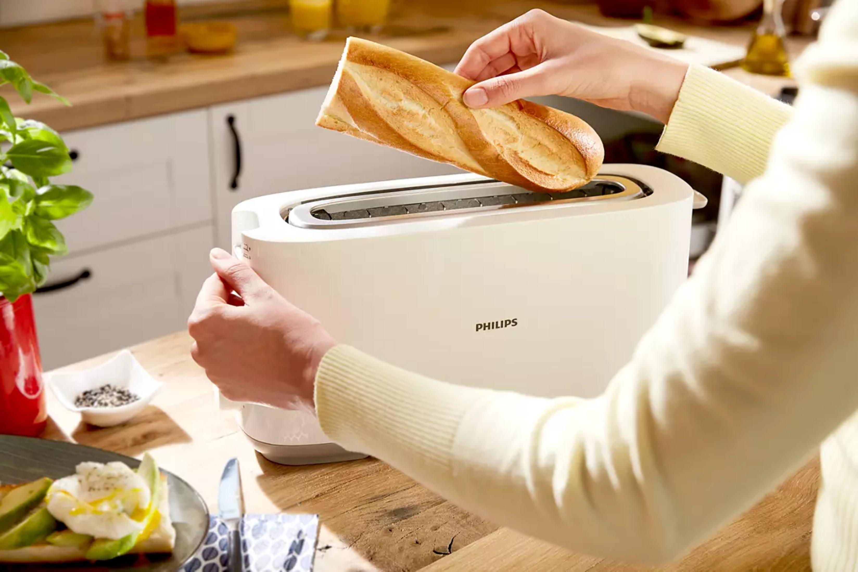 Eine Person steckt ein Baguette in einen weißen Toaster.