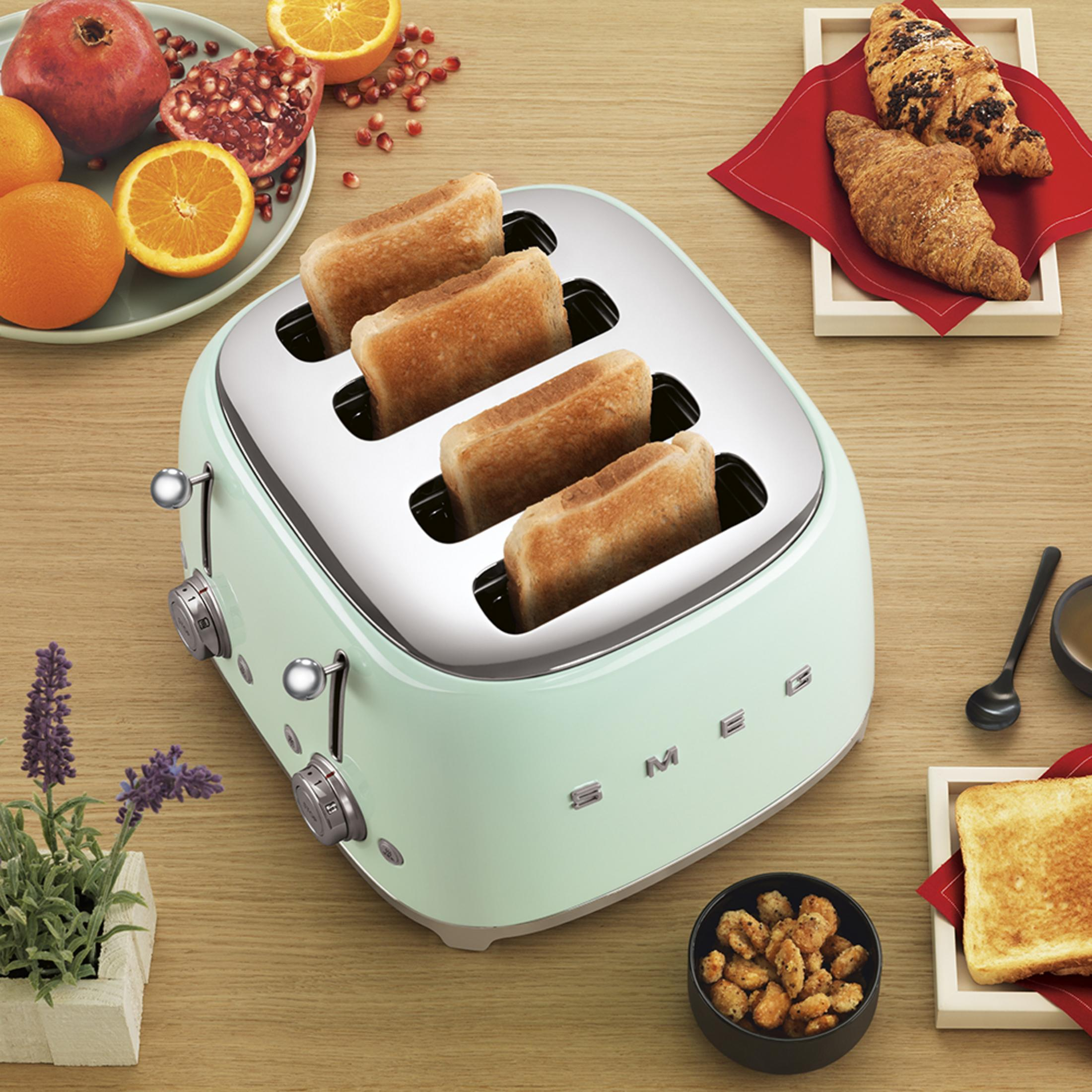 Ein mintgrüner Toaster mit vier Scheiben Toastbrot, daneben Früchte und Croissants.