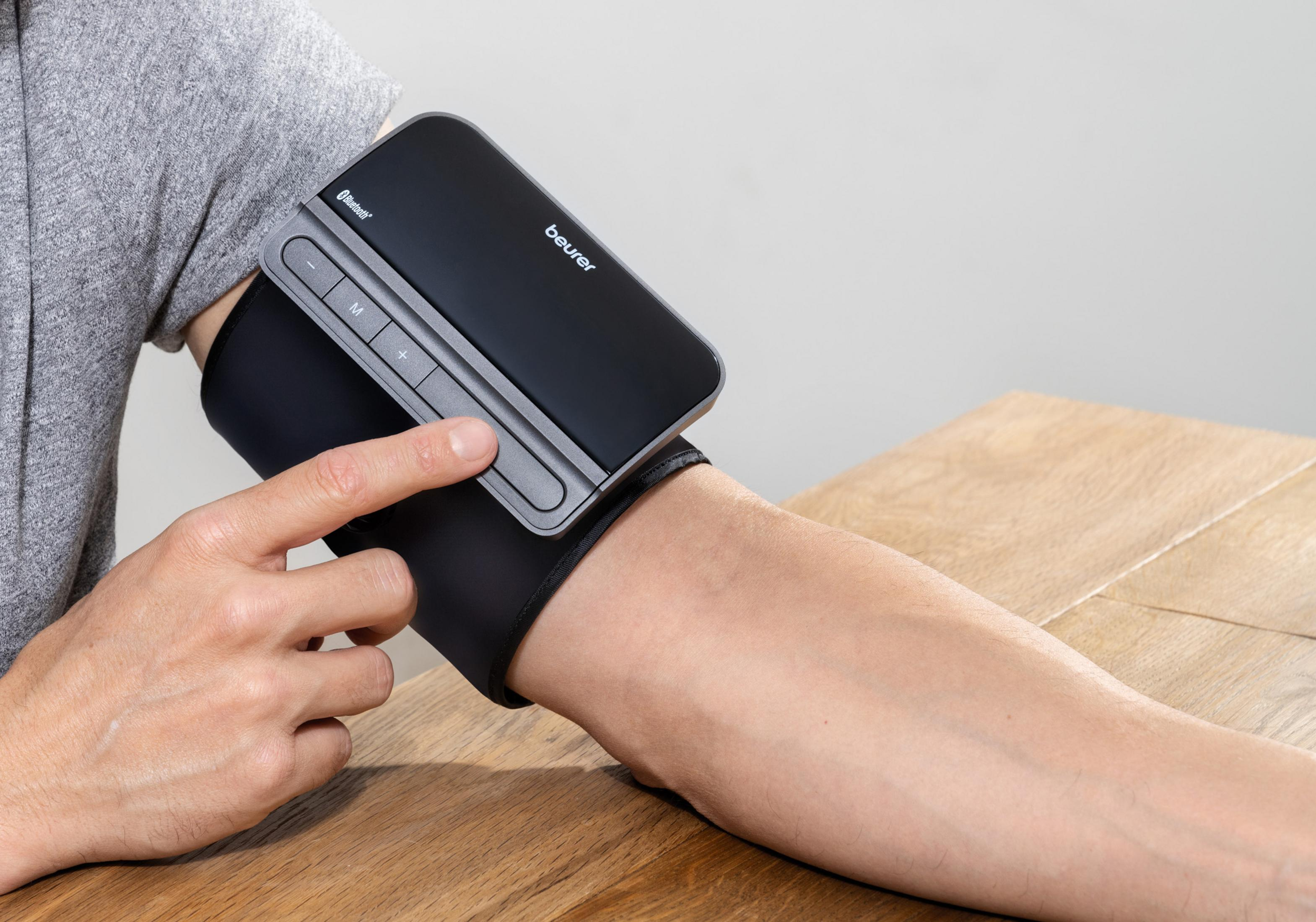 Person misst Blutdruck am Arm mit Beurer-Gerät auf Holztisch.