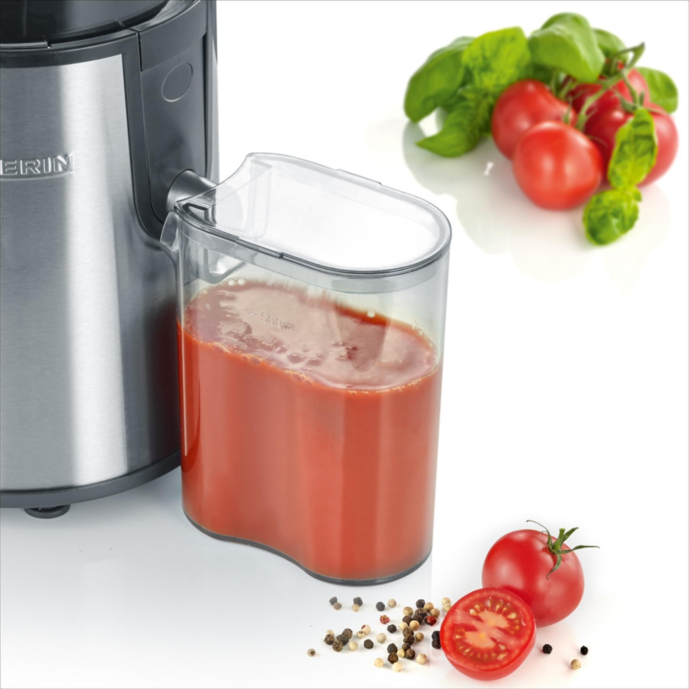 Ein Entsafterbehälter mit Tomatensaft neben Tomaten, Basilikum und Pfefferkörnern.