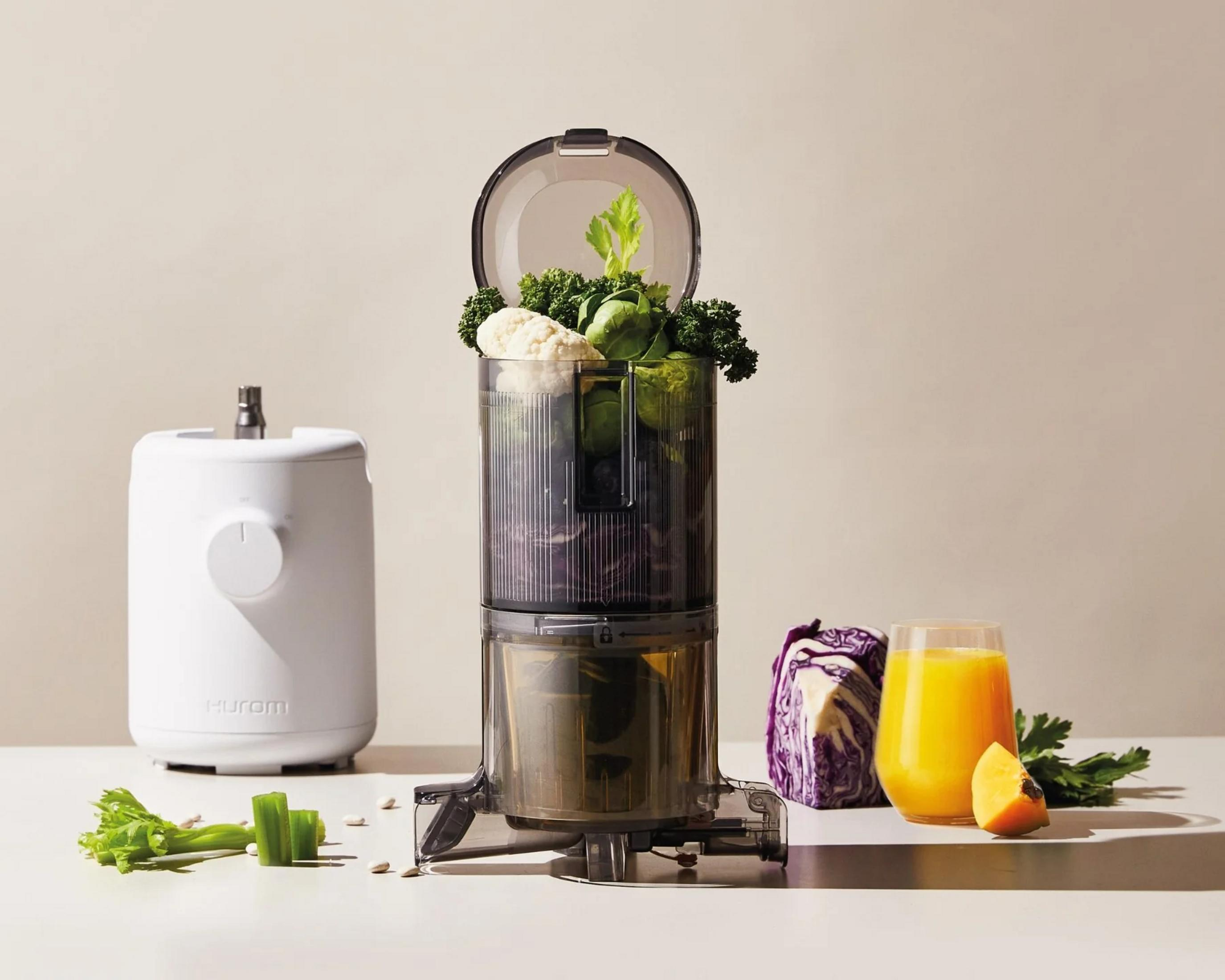 Ein Entsafter mit Gemüse, Saft und einer weißen Maschine daneben.