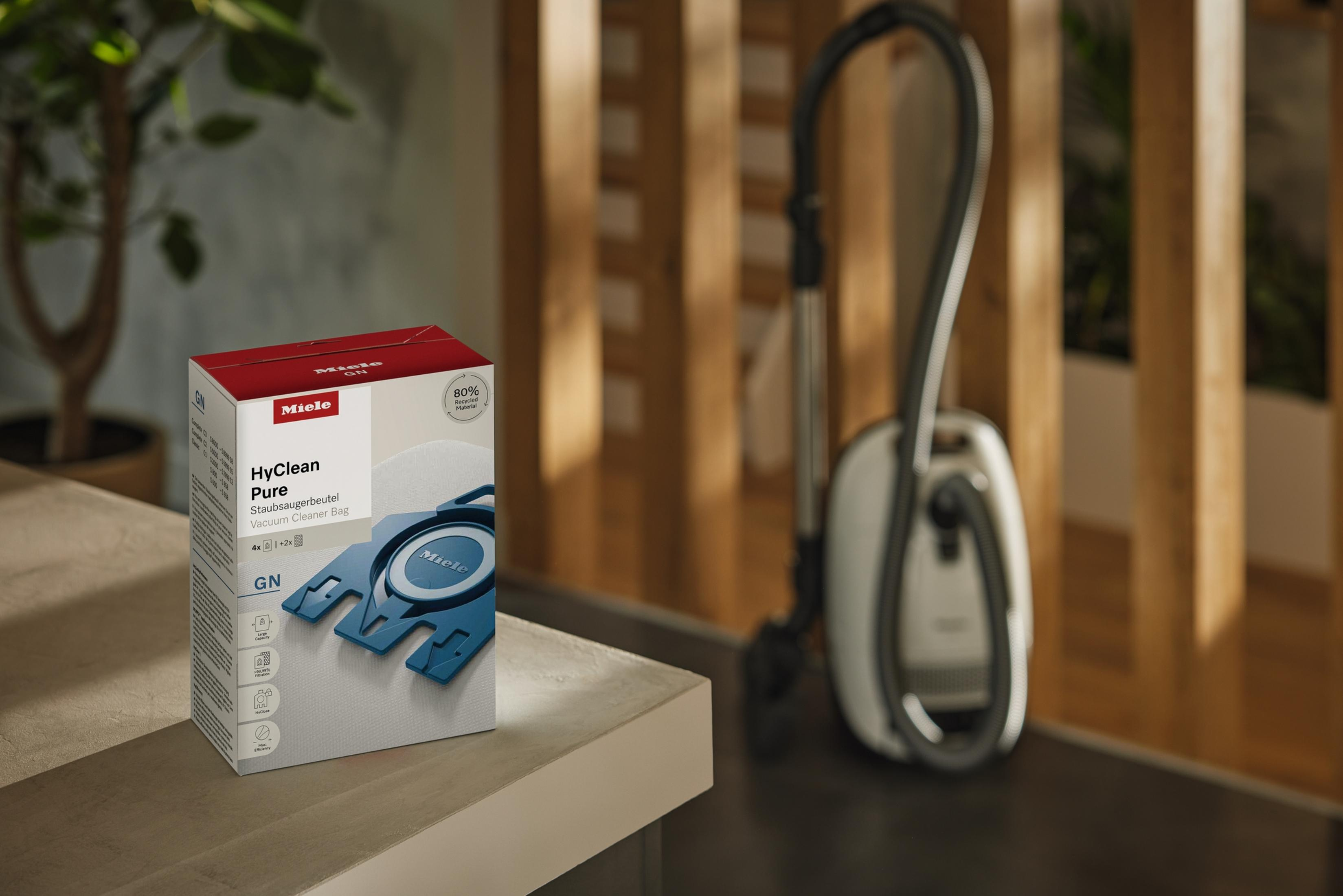 Miele HyClean Pure Staubsaugerbeutel sind auf einem Tisch mit einem Staubsauger im Hintergrund.