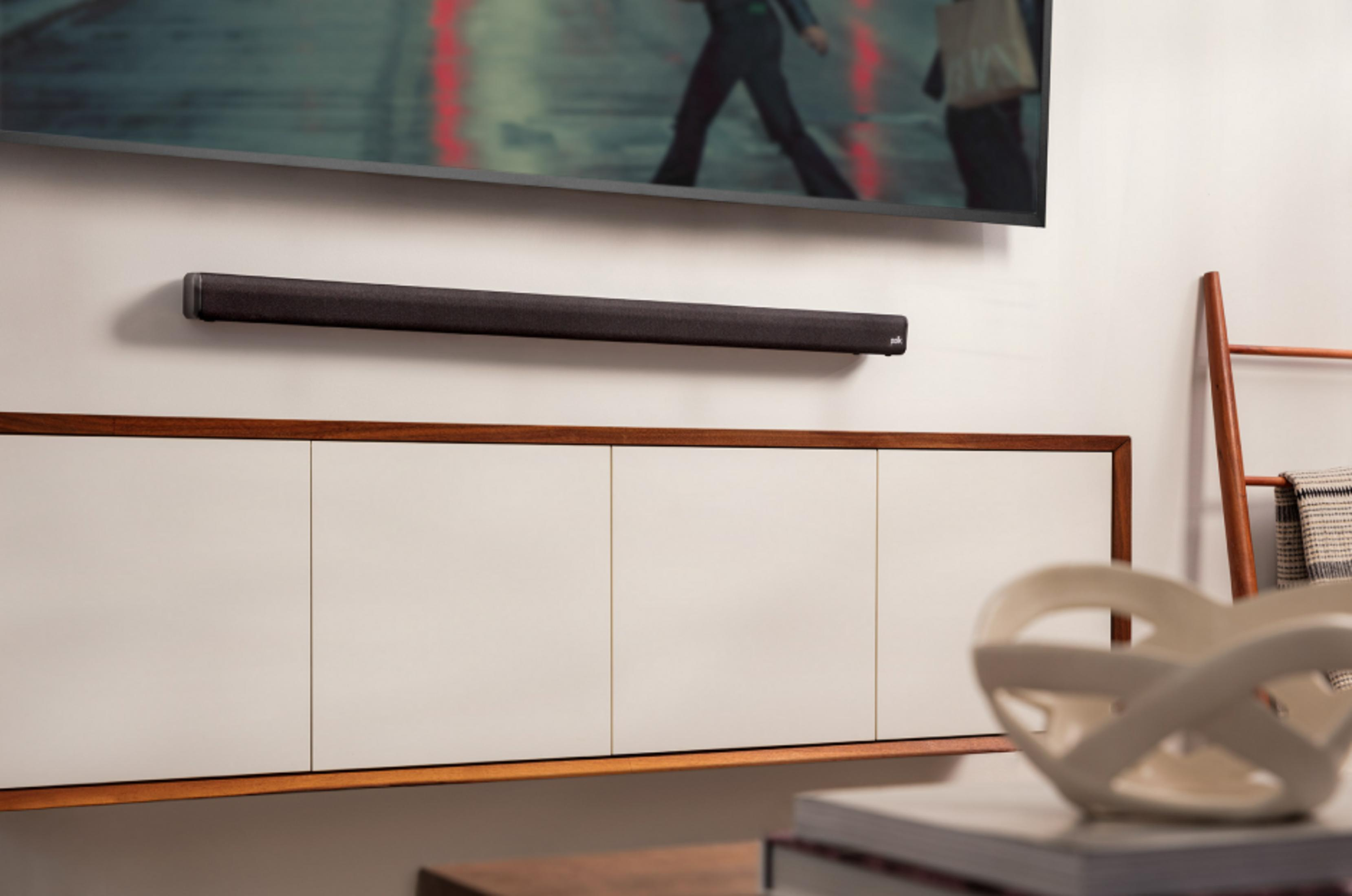 Ciemny soundbar zamontowany pod telewizorem, nad białą szafką.