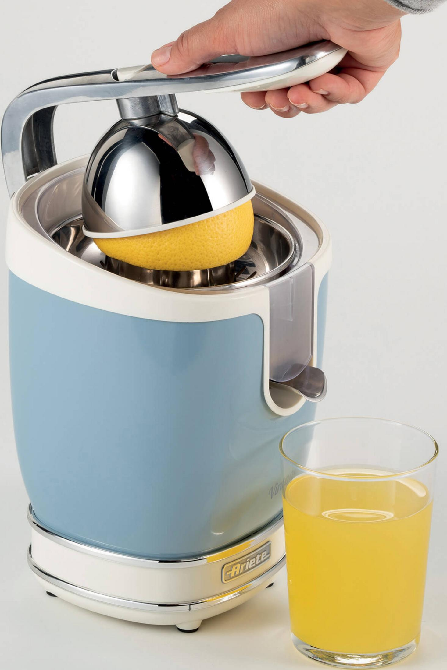 Eine Hand drückt den Griff eines Entsafters mit einer Zitrone und einem Glas Saft.