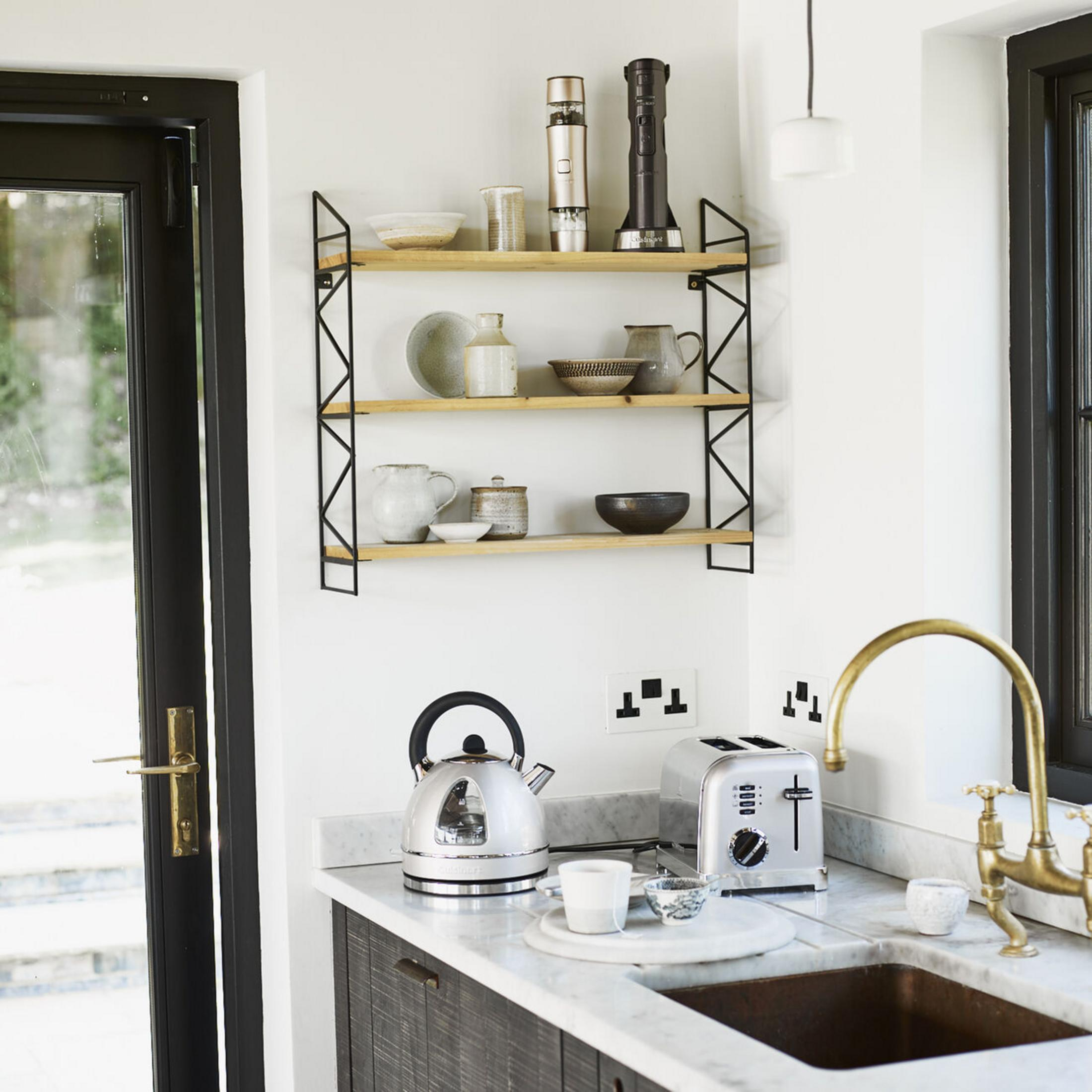 Cucina moderna con elettrodomestici argentati, mensole in legno e rubinetto in ottone.