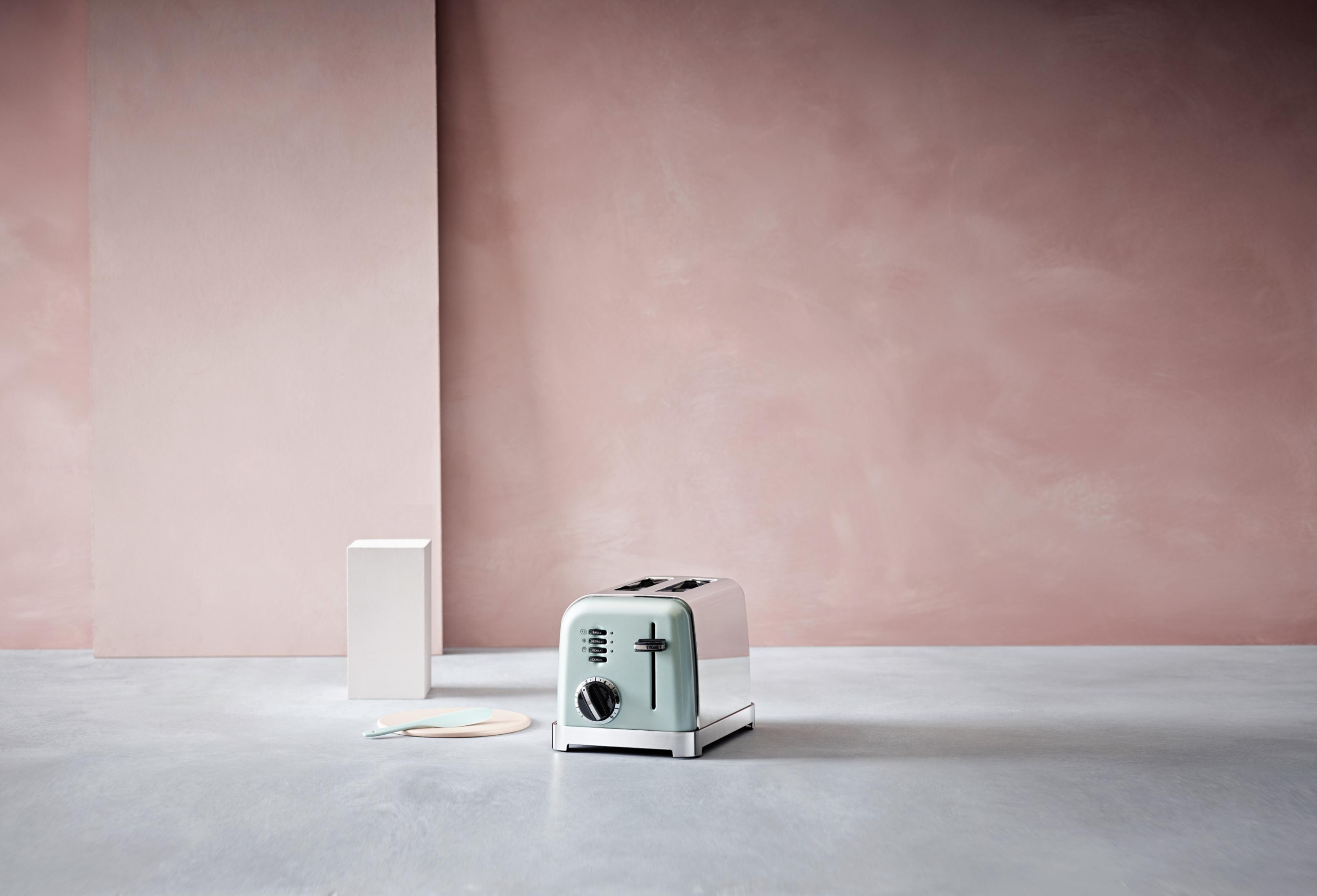 Jasnozielony toster na szarej powierzchni przed różową ścianą.