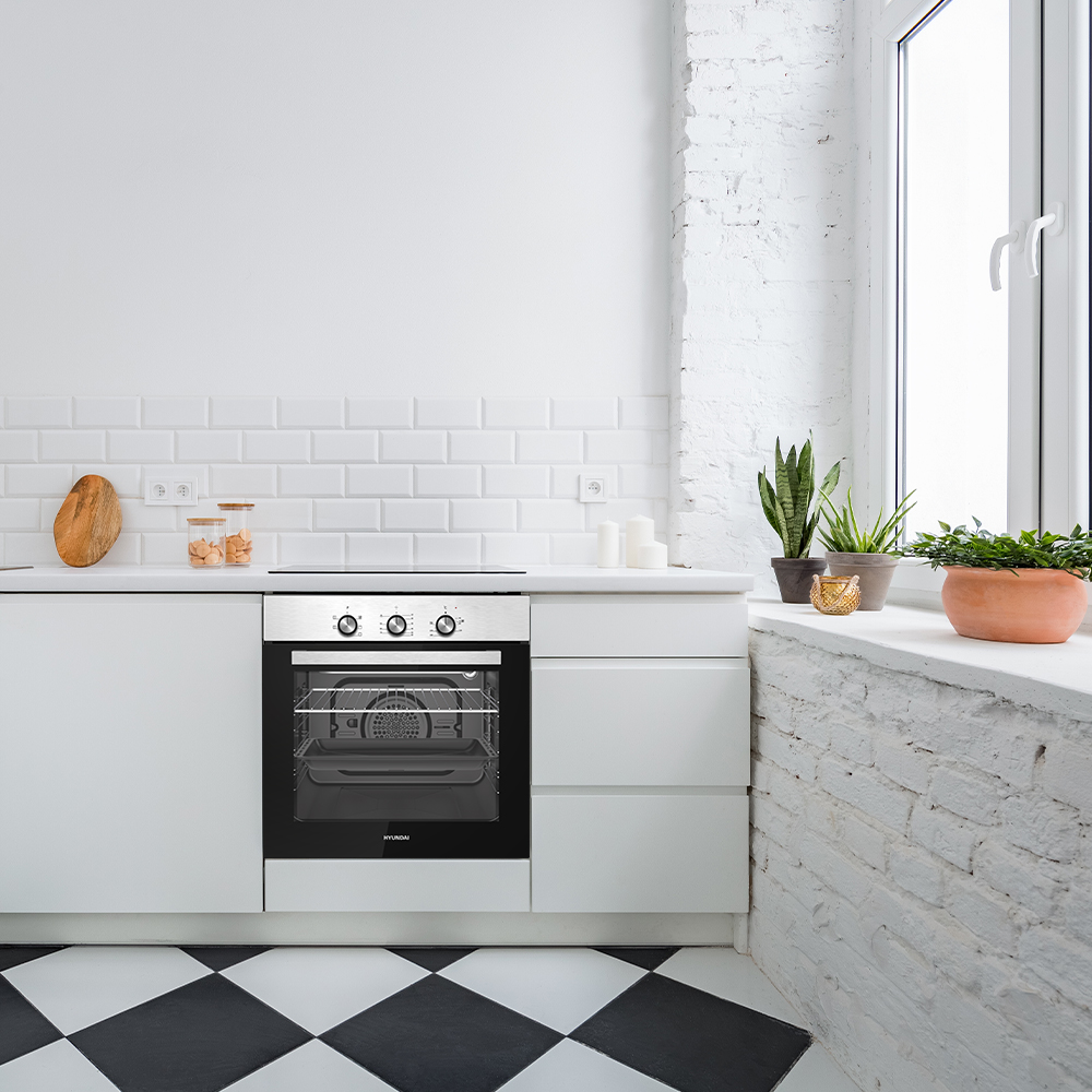 Moderna cocina blanca con horno de acero inoxidable, salpicadero de azulejos y alféizar con plantas.