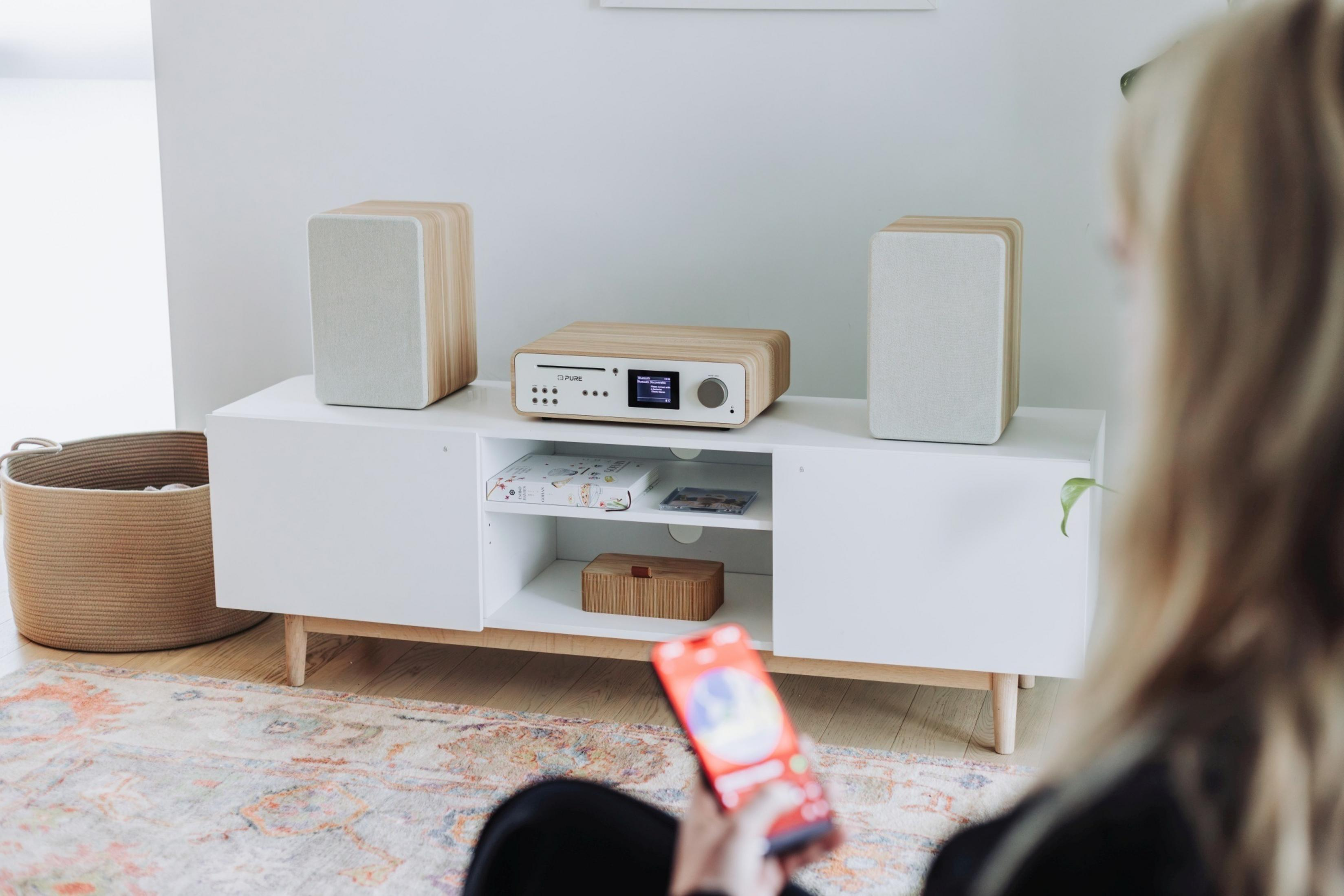 Impianto stereo in legno con due altoparlanti su mobile bianco, persona che tiene un telefono.