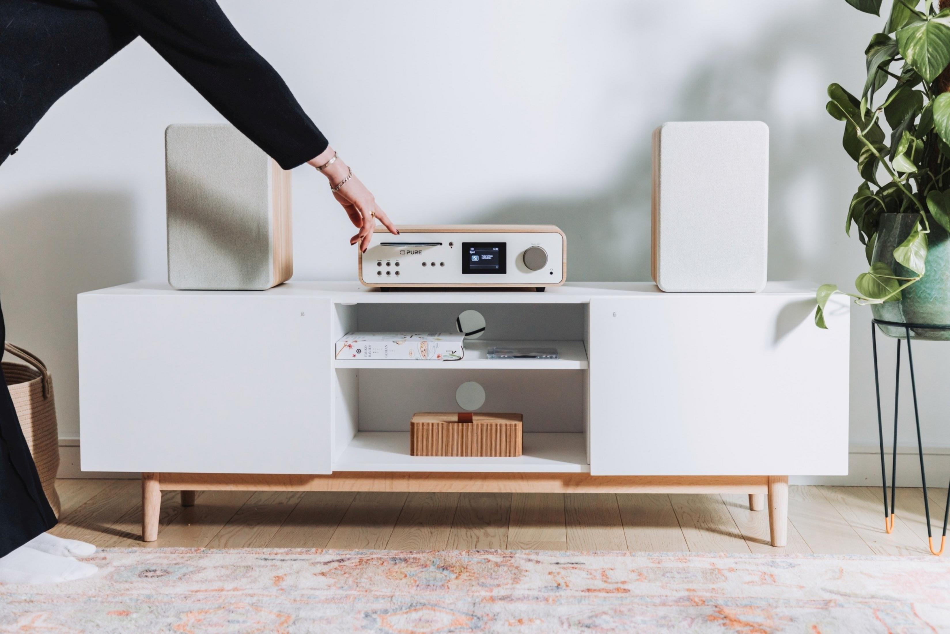 Una mano aziona un sistema hi-fi bianco con accenti in legno su un mobile bianco.