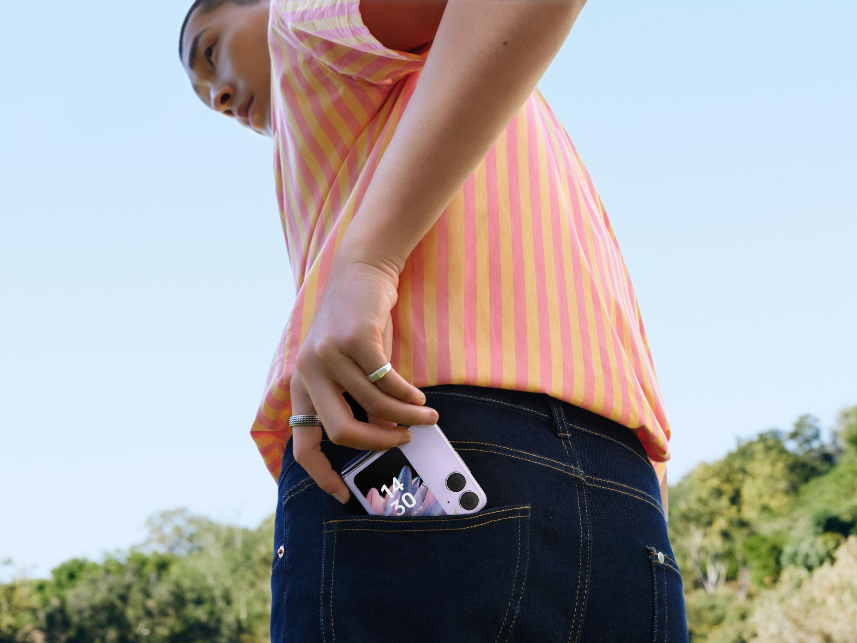Una persona mette un telefono flip viola nella tasca dei jeans.