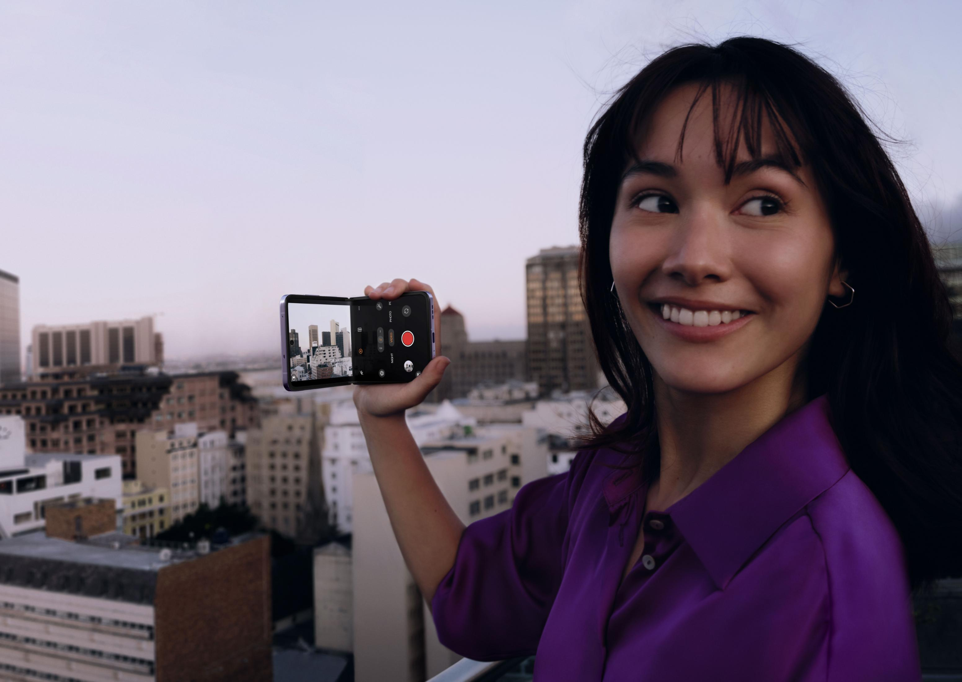 Donna filma lo skyline della città al tramonto con un telefono pieghevole.