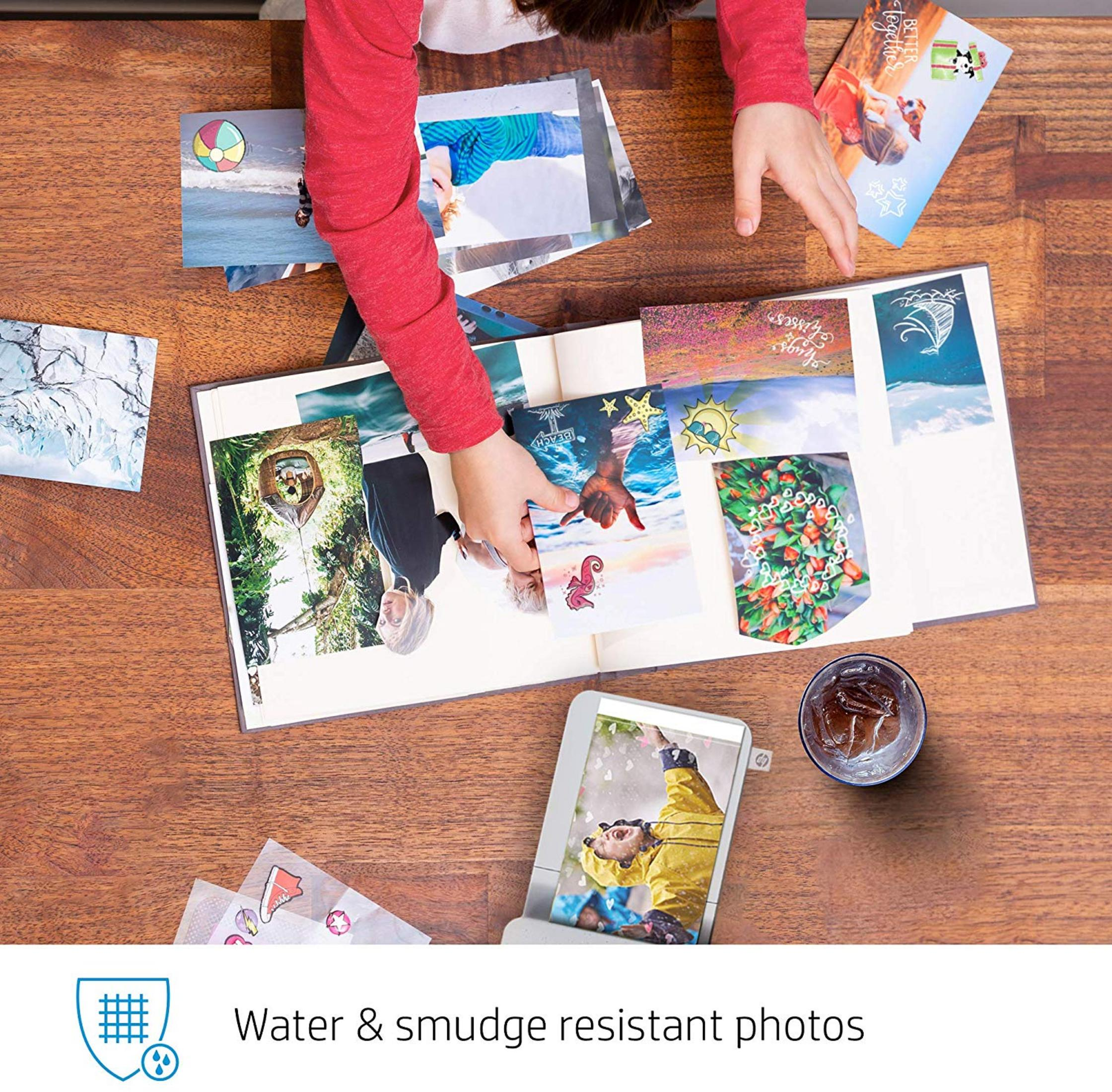 Dziecko wkłada zdjęcia do albumu. Widoczna drukarka i szklanka napoju.