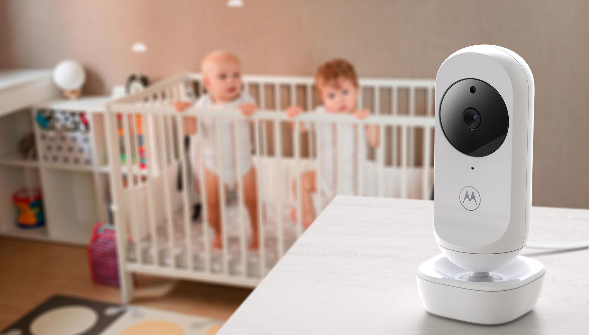 Ein Babyphone mit Motorola-Logo steht auf einem Tisch vor einem Kinderbett mit zwei Babys.