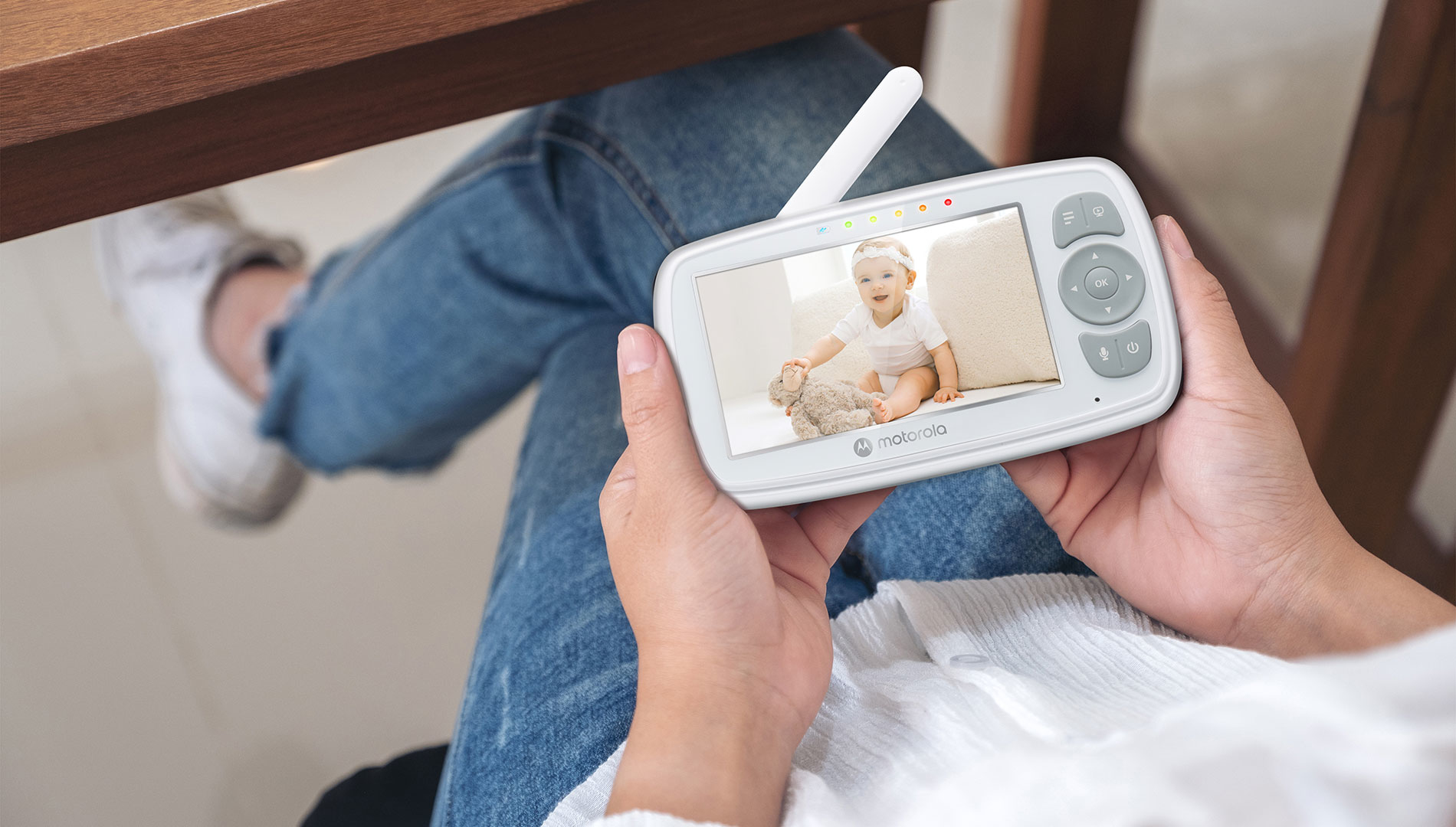 Person hält Babyfon mit lächelndem Baby und Teddybär.