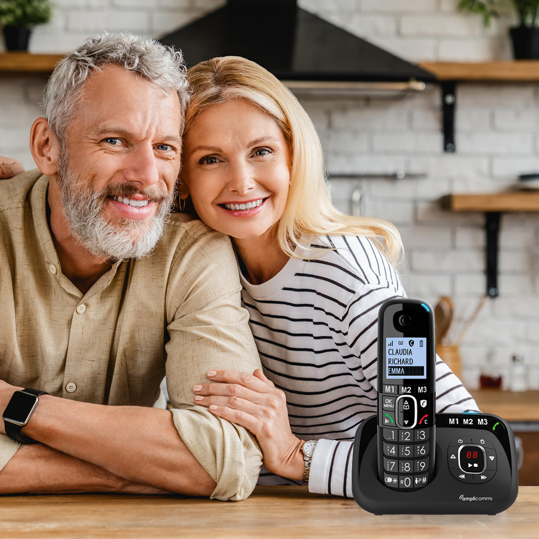 Een ouder echtpaar glimlacht naar de camera, met een telefoon ernaast.