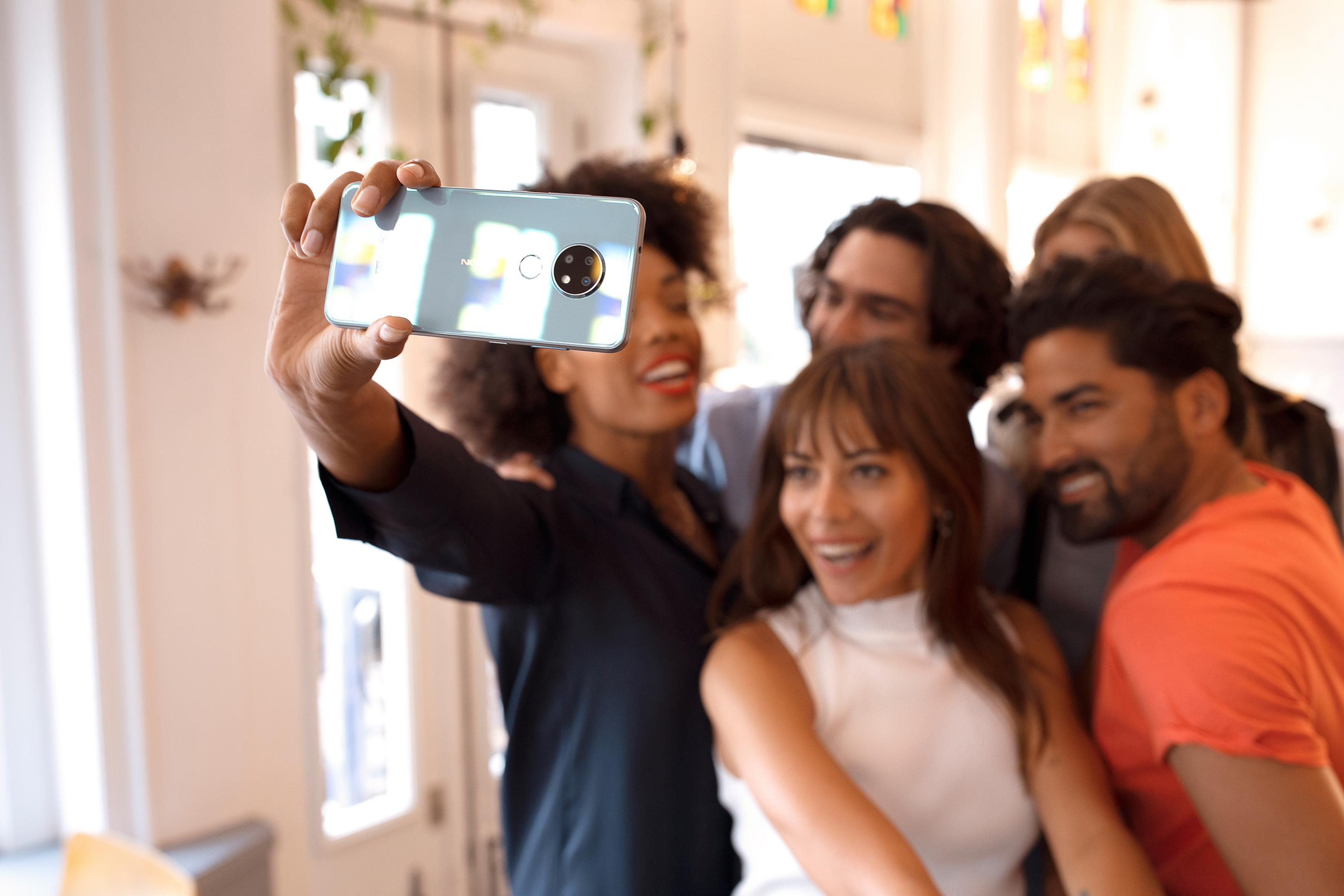 Eine Gruppe von Freunden macht ein Selfie mit einem hellblauen Smartphone in einem Innenraum.