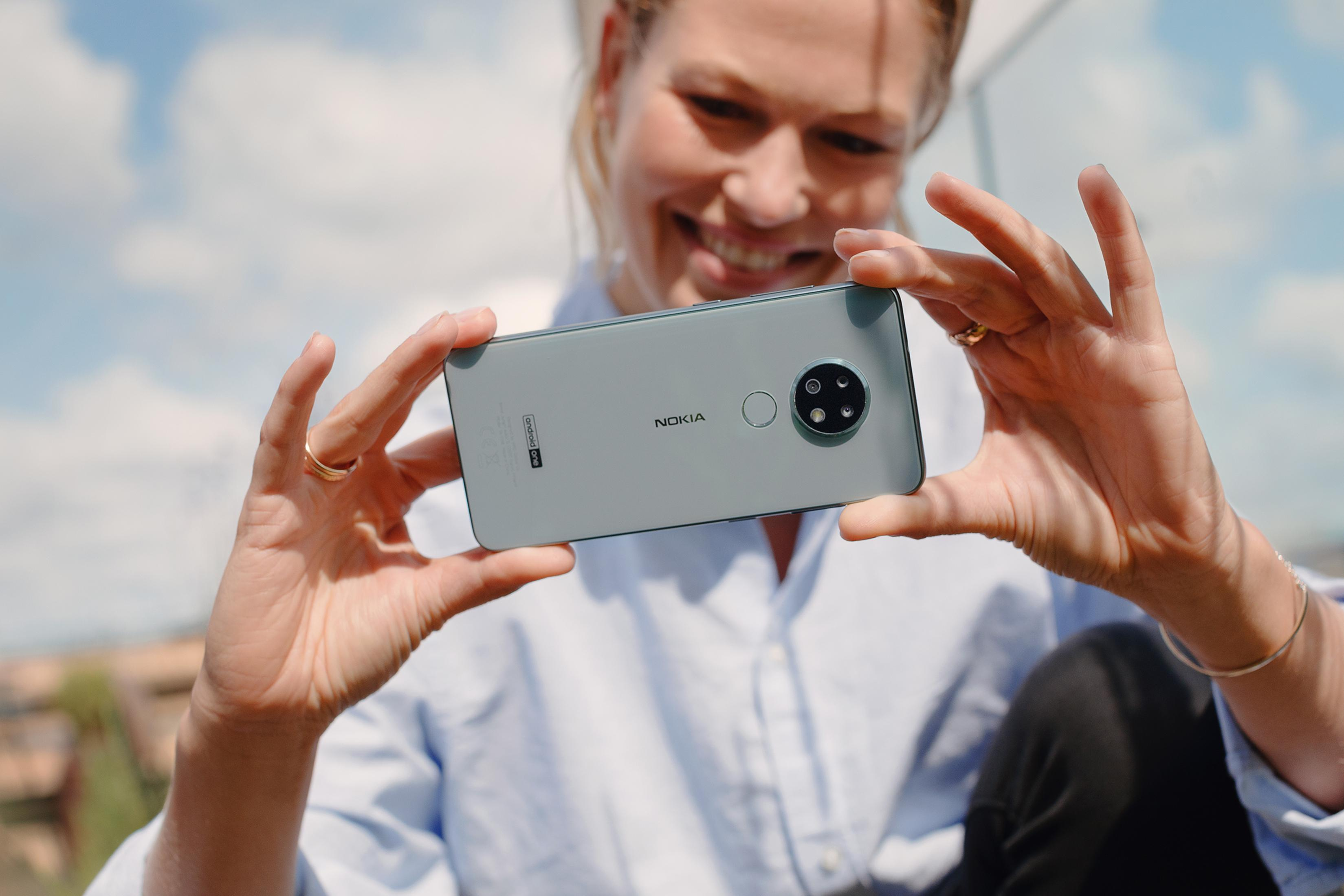 Frau hält ein hellgraues Nokia-Smartphone mit dreifacher Kamera.