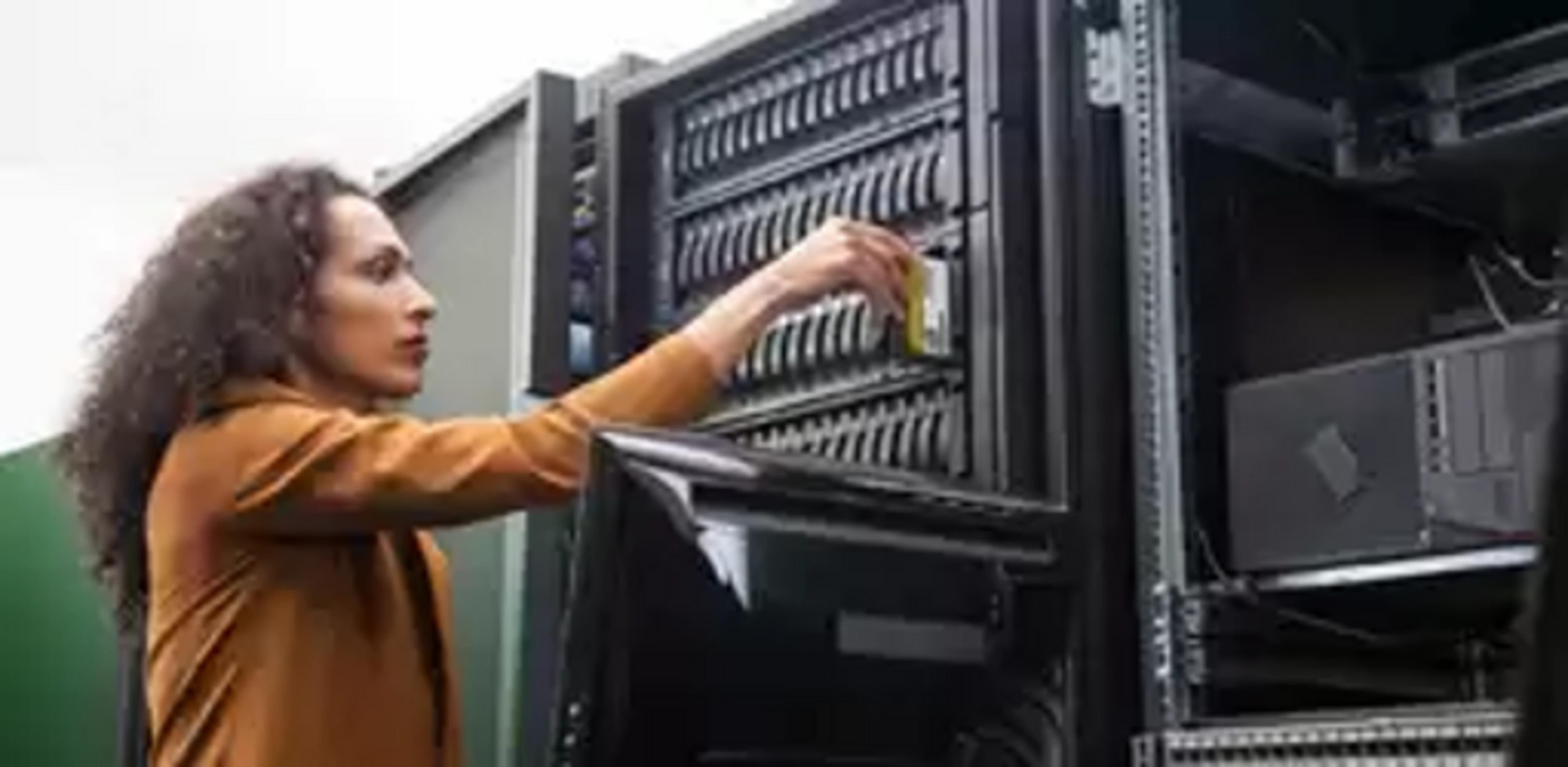 Kobieta z kręconymi włosami wkłada żółty dysk do szafy serwerowej.