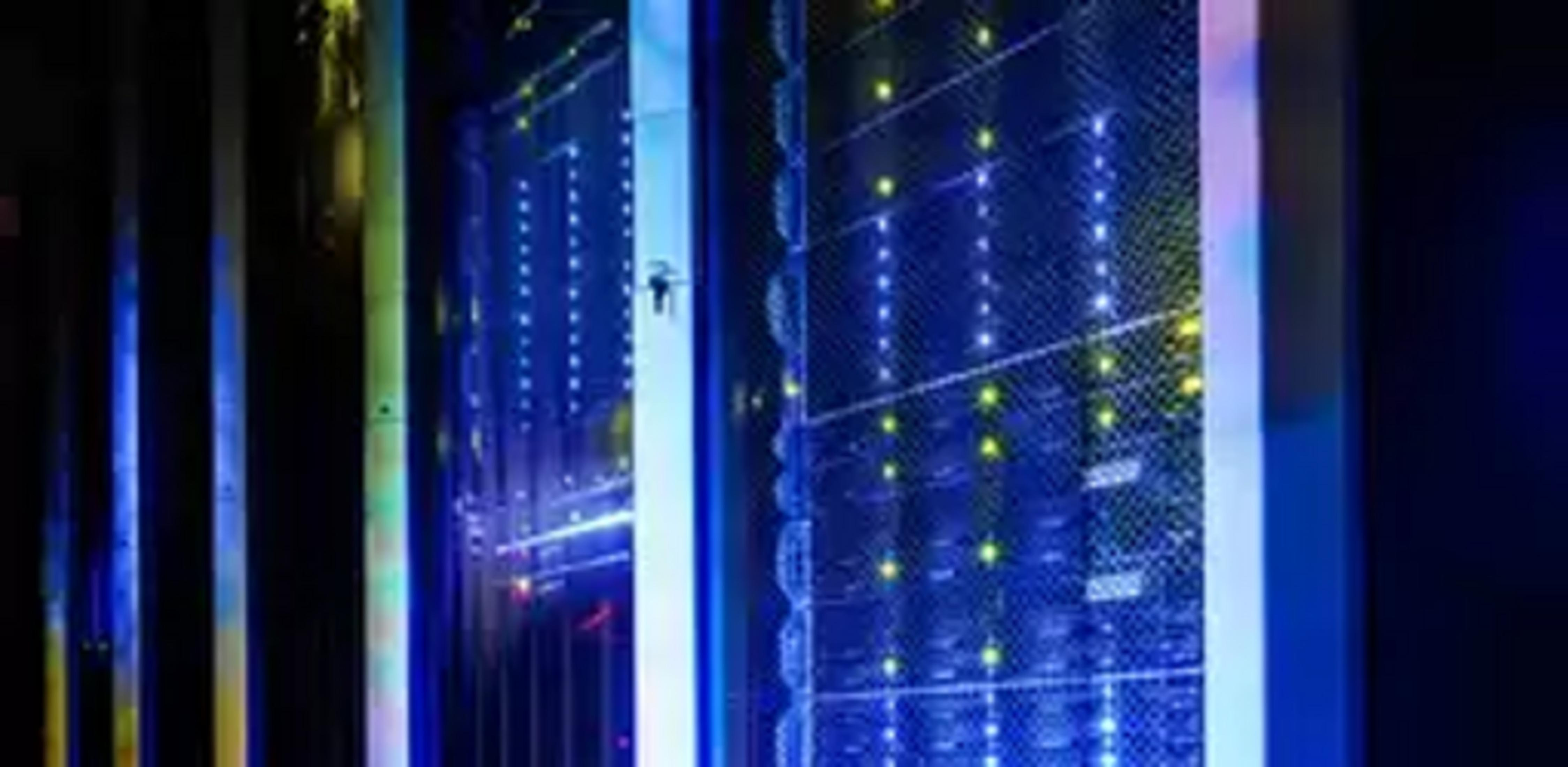 Szafy serwerowe z niebieskimi i żółtymi światłami w ciemnym pomieszczeniu.