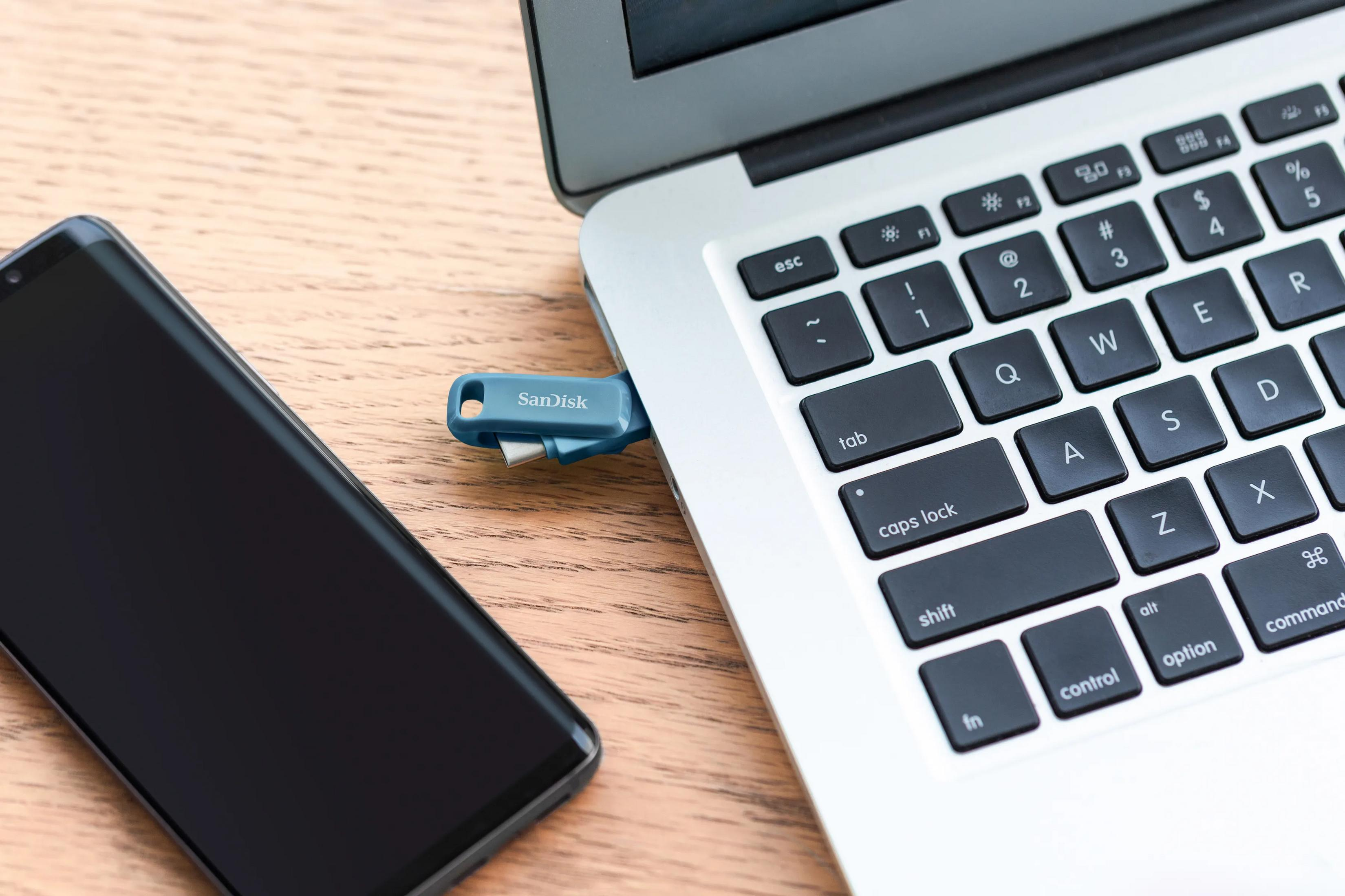 Pendrive jest podłączony do laptopa obok smartfona.