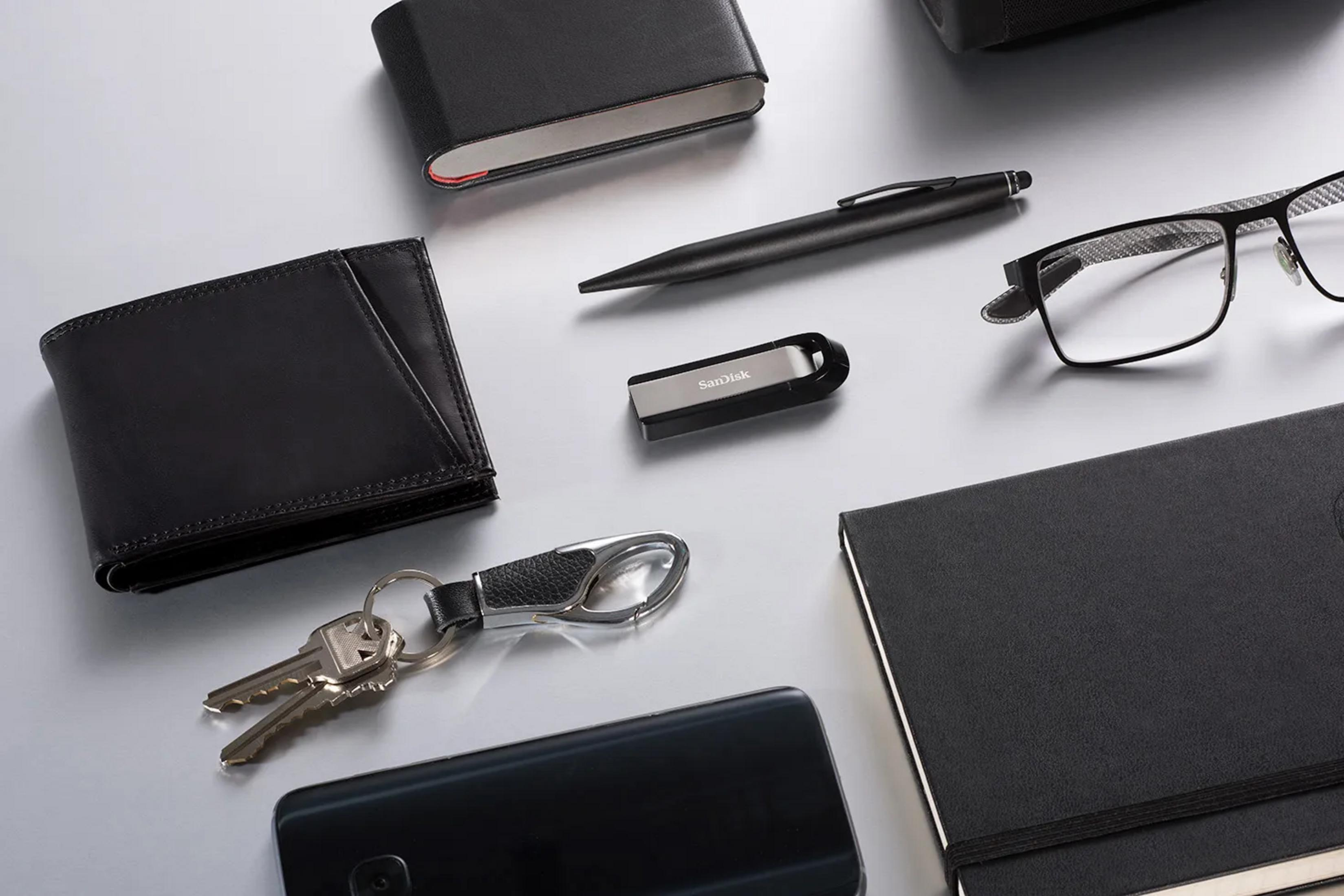 Czarny portfel, klucze, telefon, długopis, okulary i notatnik na stole.