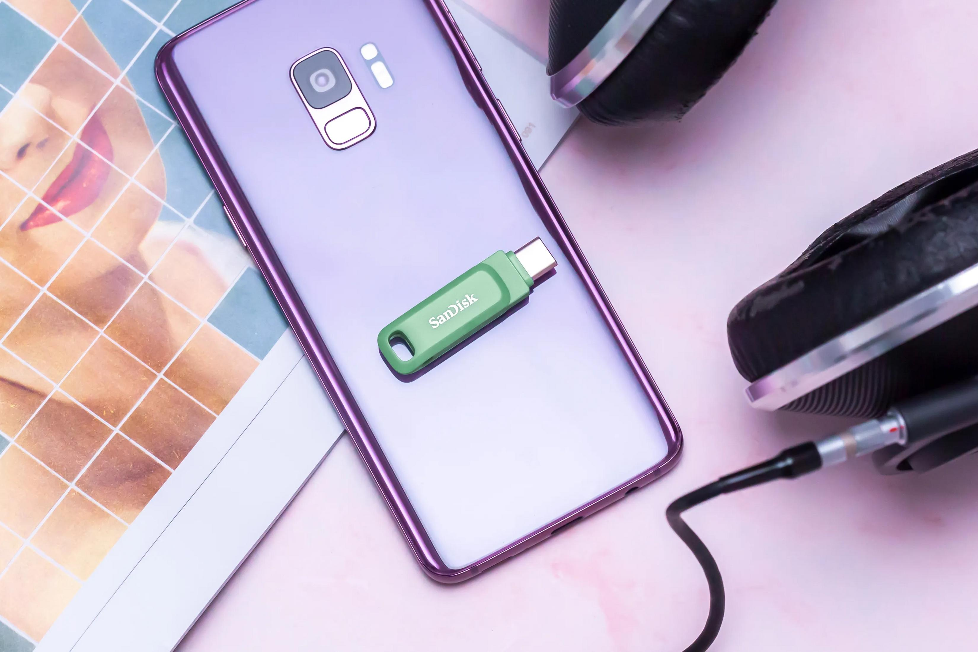 Paarse smartphone met groene USB-stick en koptelefoon op lichte achtergrond.