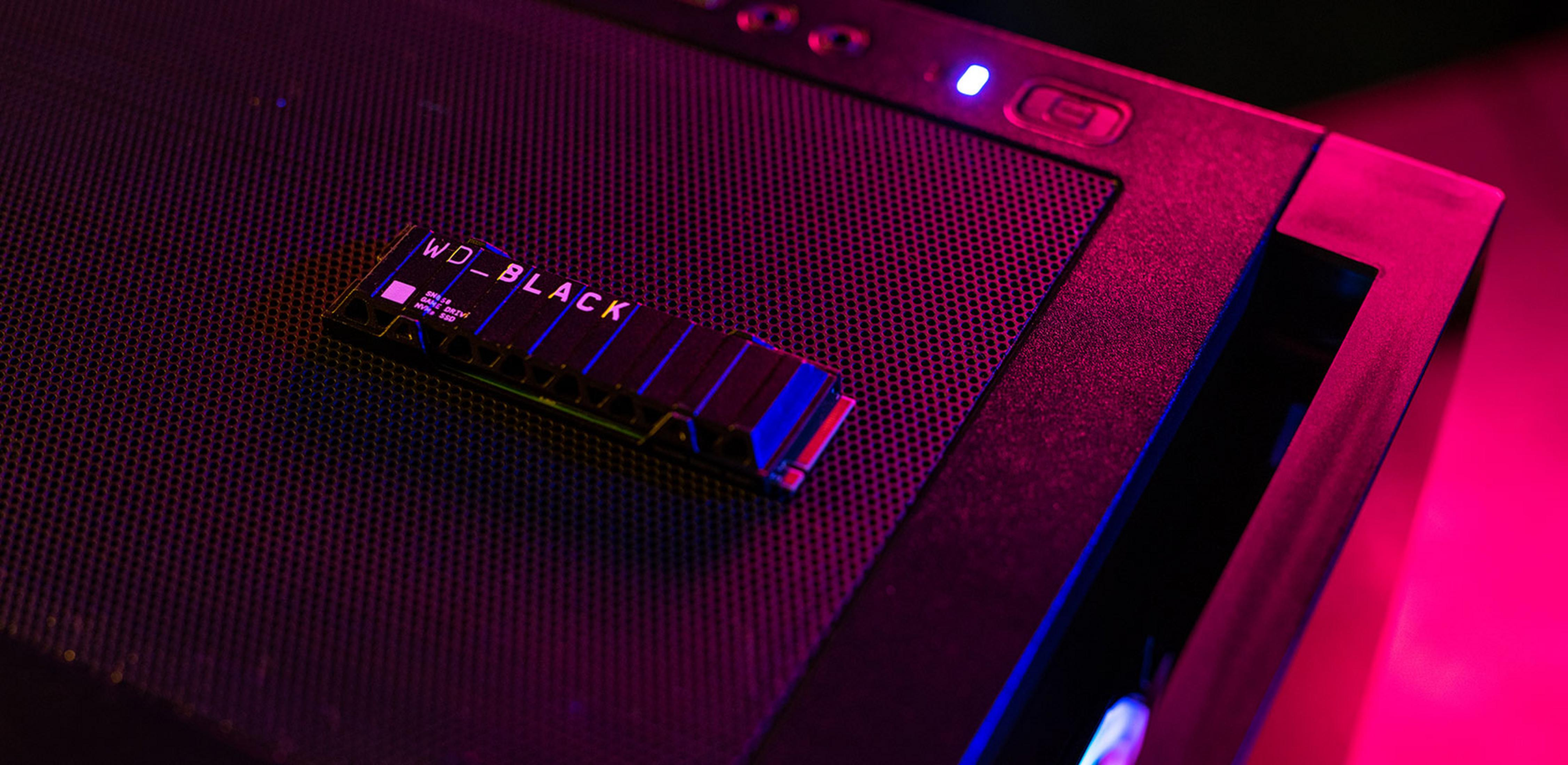 Dysk SSD NVMe WD_BLACK na ciemnej, perforowanej powierzchni, oświetlony różowym i niebieskim światłem.