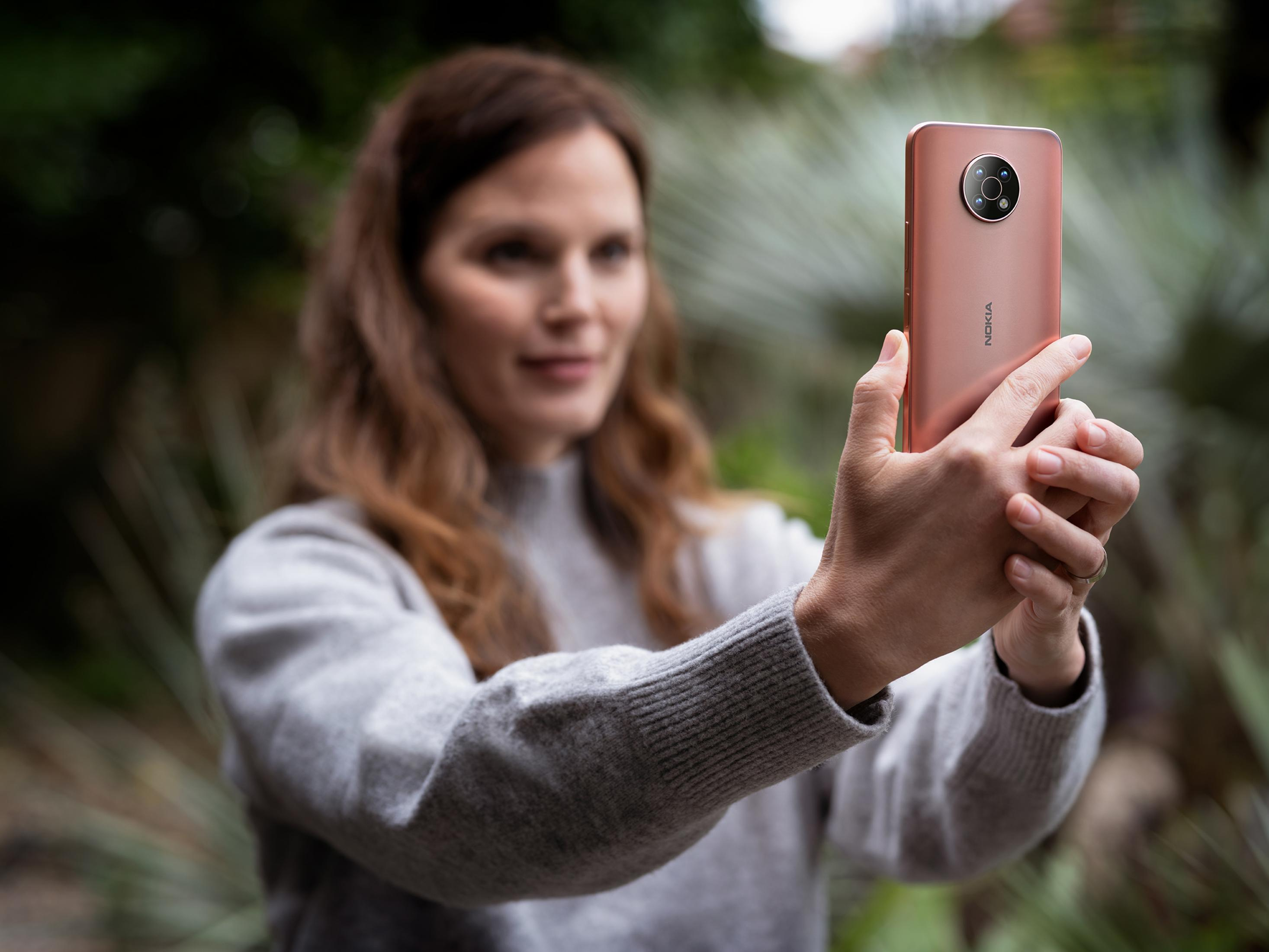 Eine Frau mit braunen Haaren hält ein rosafarbenes Nokia-Smartphone.