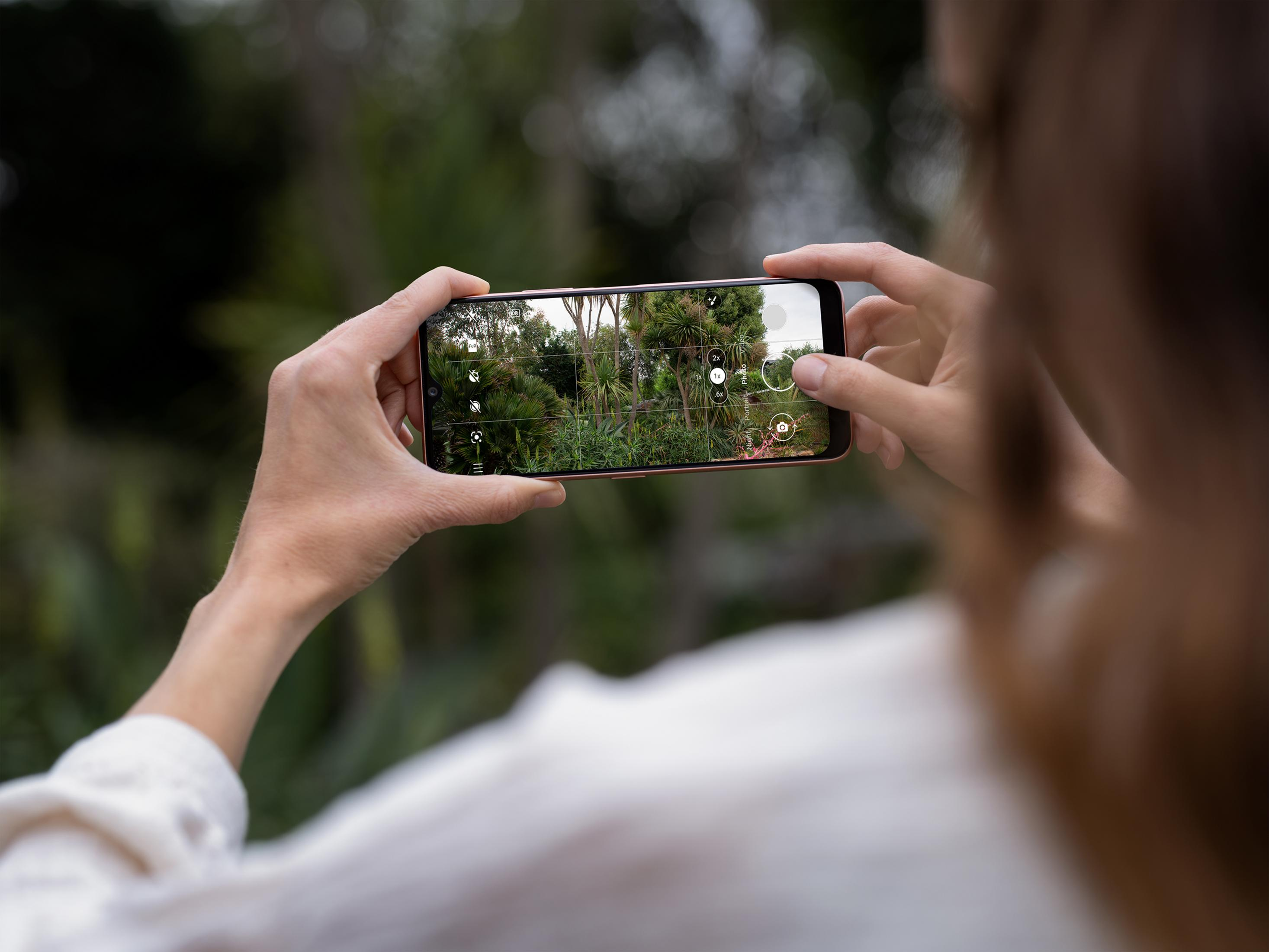 Hände halten ein Smartphone, das eine grüne Gartenlandschaft aufnimmt.