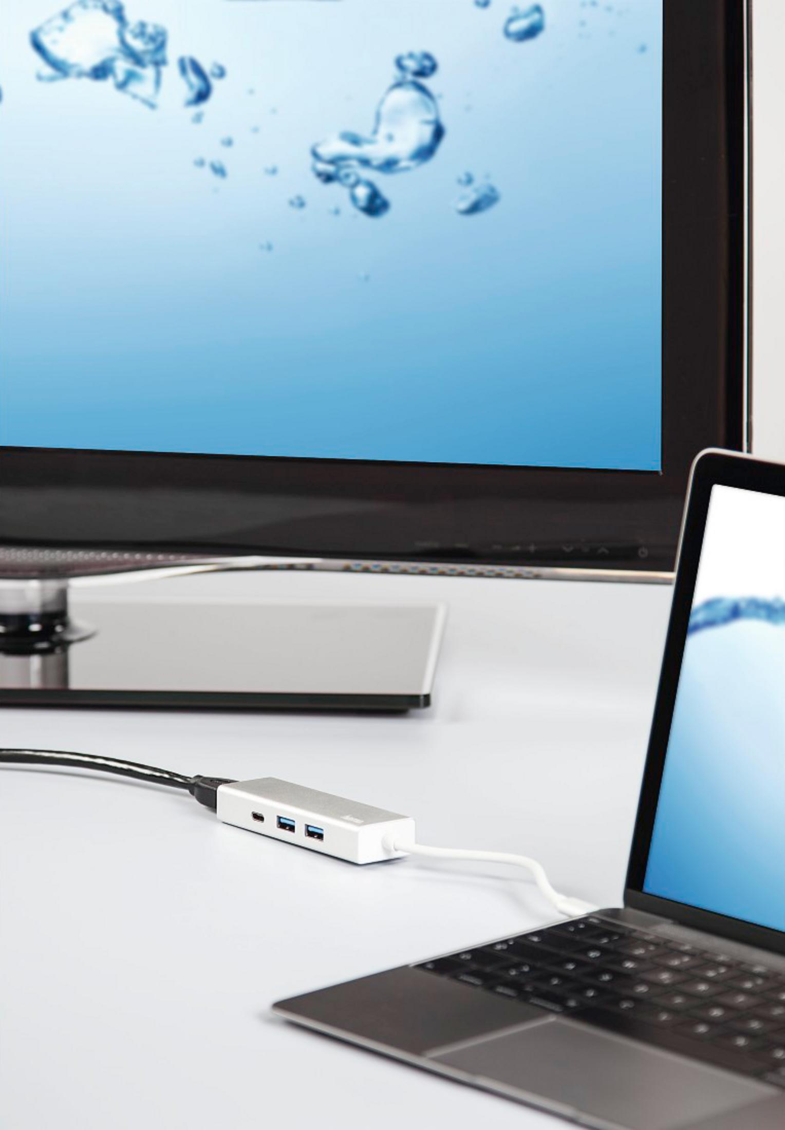 Ein silberner USB-C-Hub ist mit einem Laptop verbunden. Ein Monitor zeigt Blasen im Wasser.