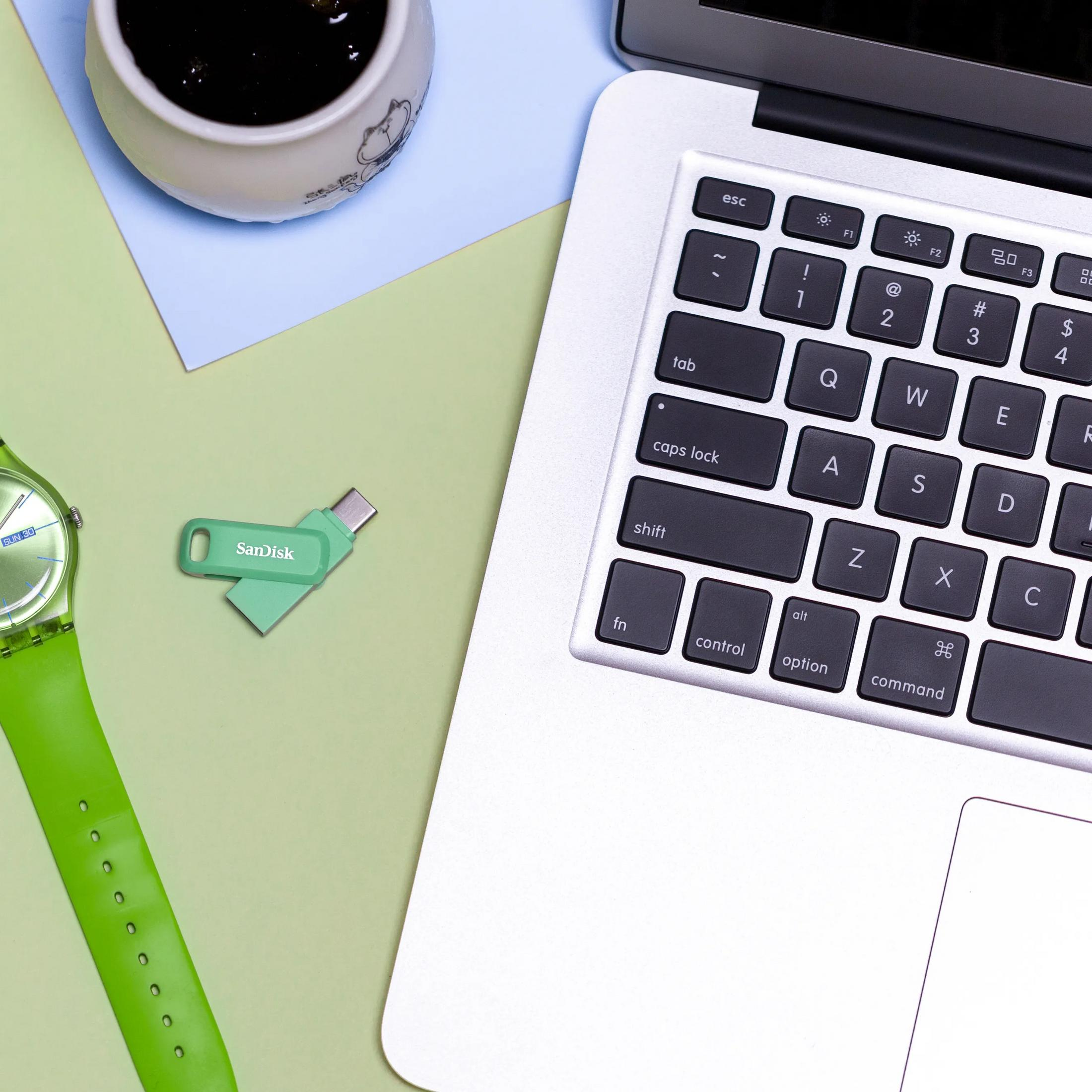 Zielony pendrive i zielony zegarek obok laptopa na kolorowym papierze.