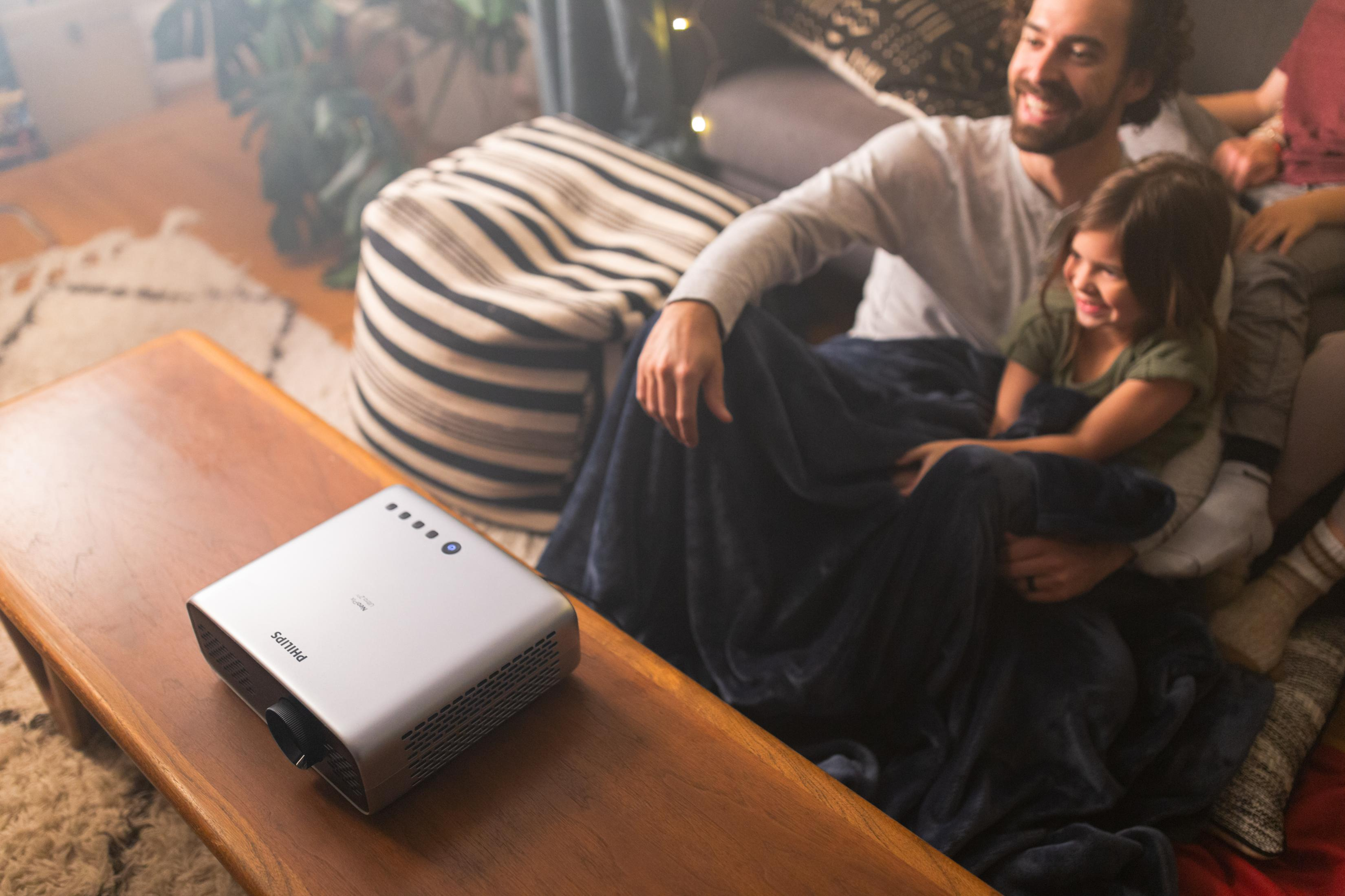 Mężczyzna i dziecko przytulają się pod kocem, projektor na stole.