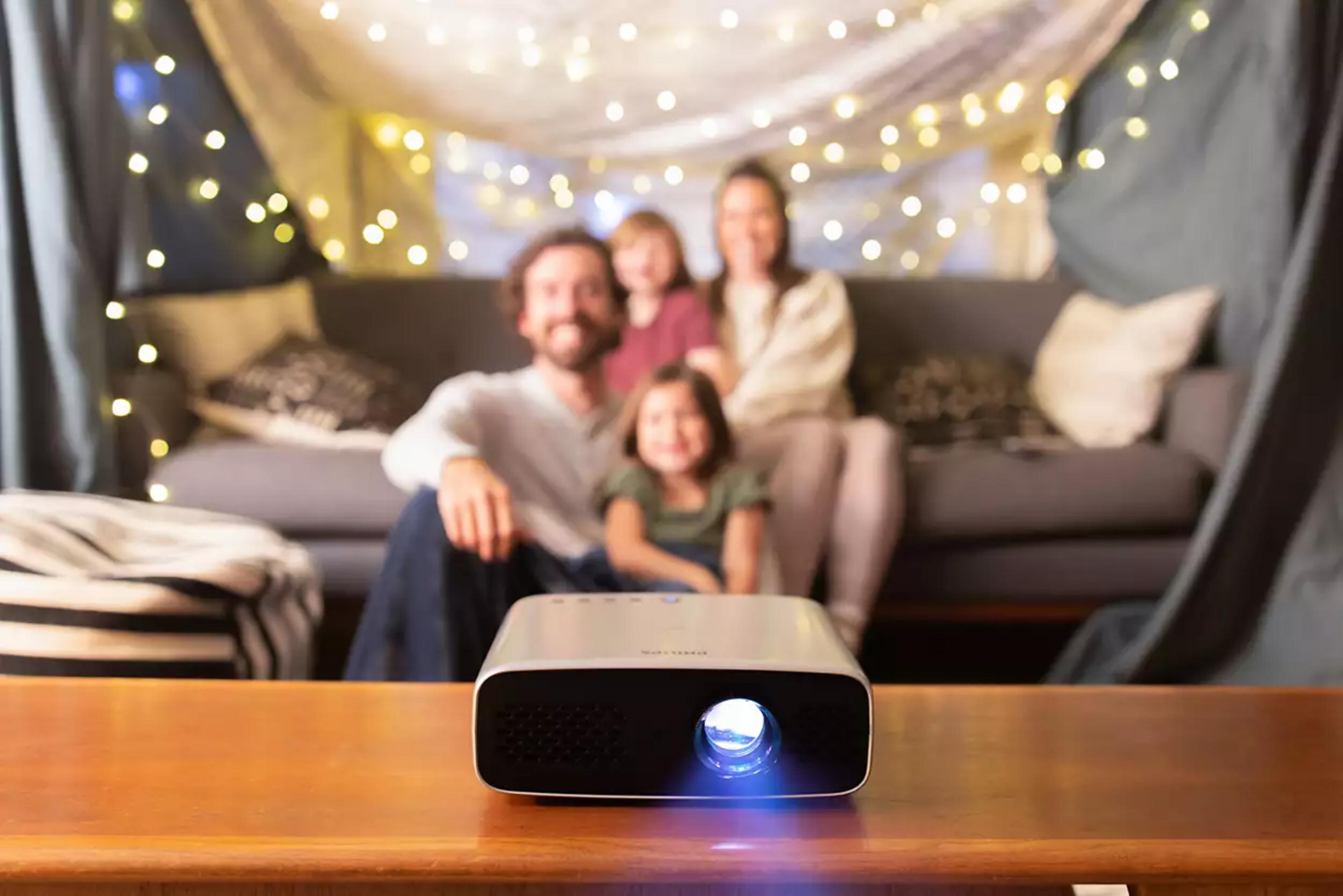 Rodzina ogląda film w improwizowanym kinie domowym z lampkami i projektorem.