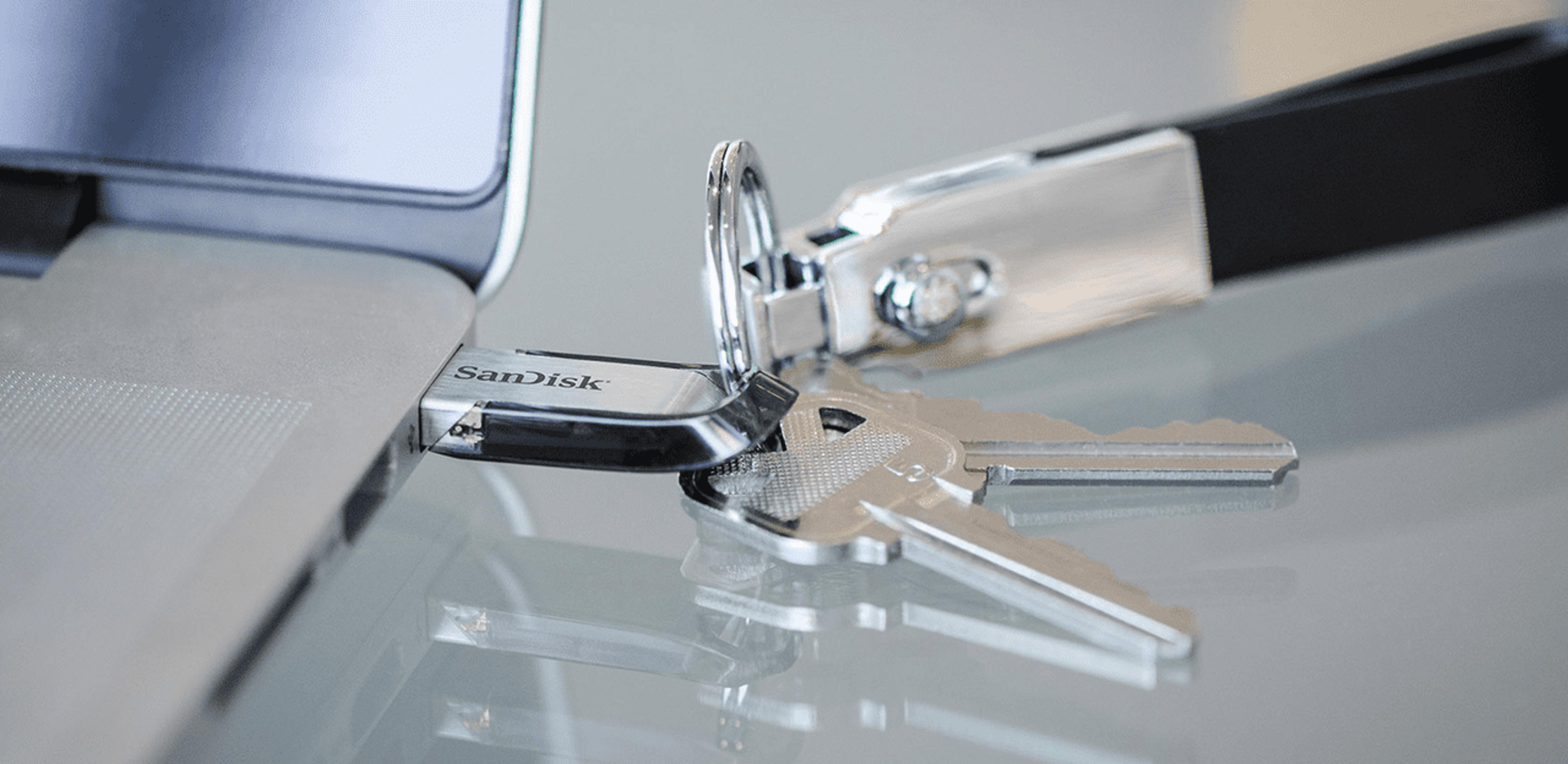 Pendrive Sandisk podłączony do laptopa, obok leżą dwa klucze.