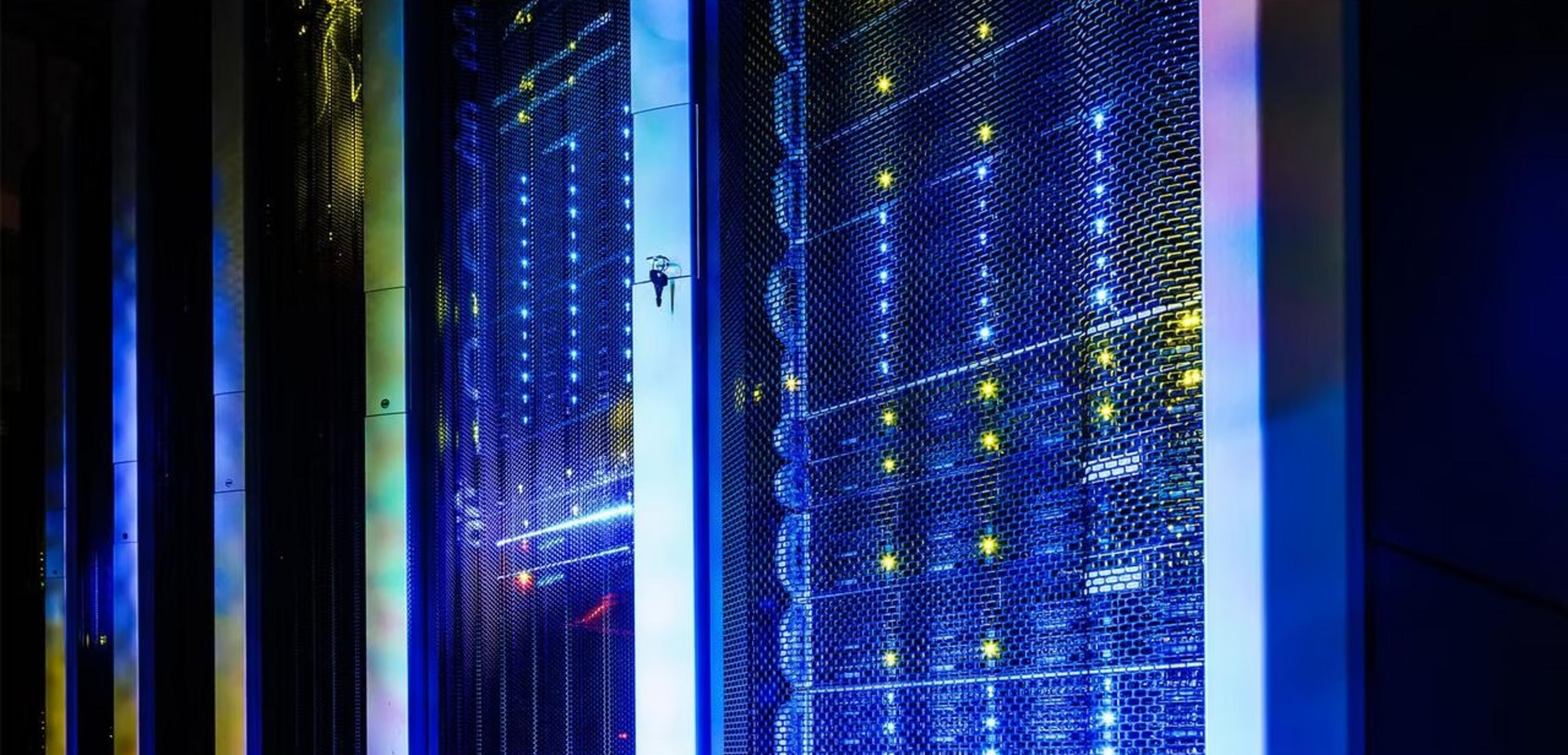 Regały serwerowe z niebieskimi i żółtymi światłami w ciemnym pomieszczeniu.