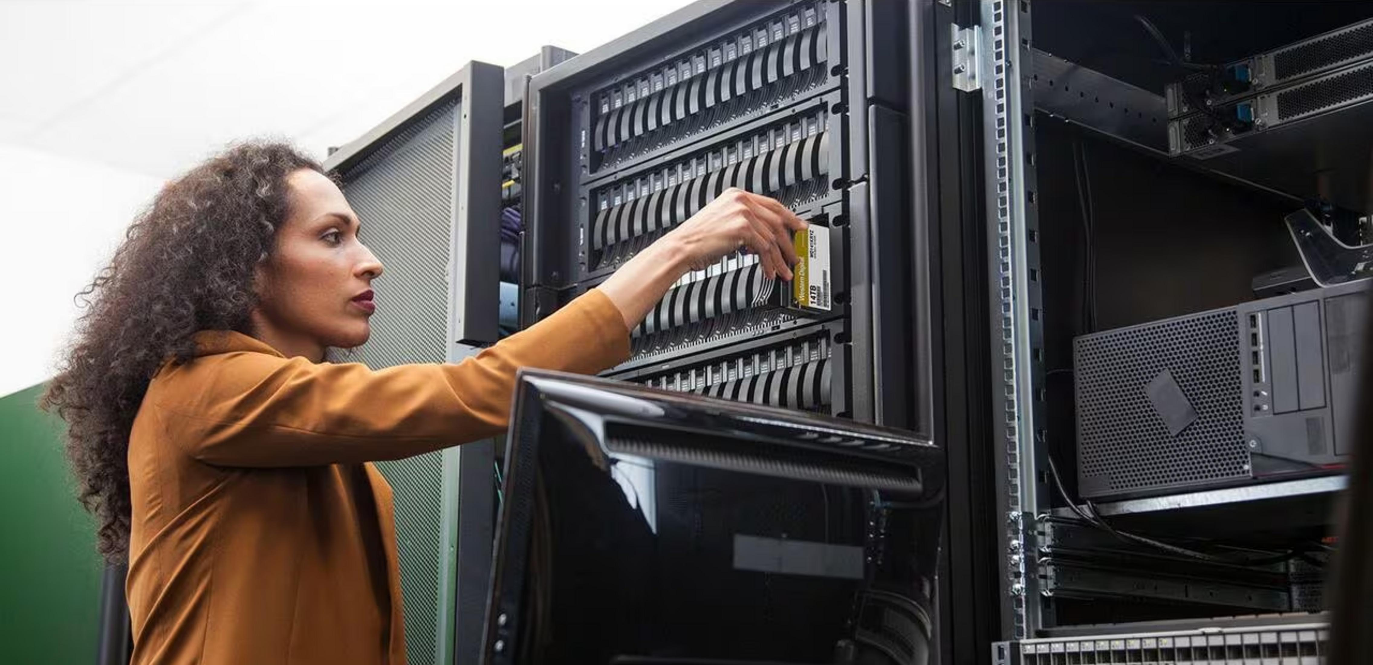 Kobieta wkłada dysk twardy do szafy serwerowej. Monitor znajduje się na pierwszym planie.