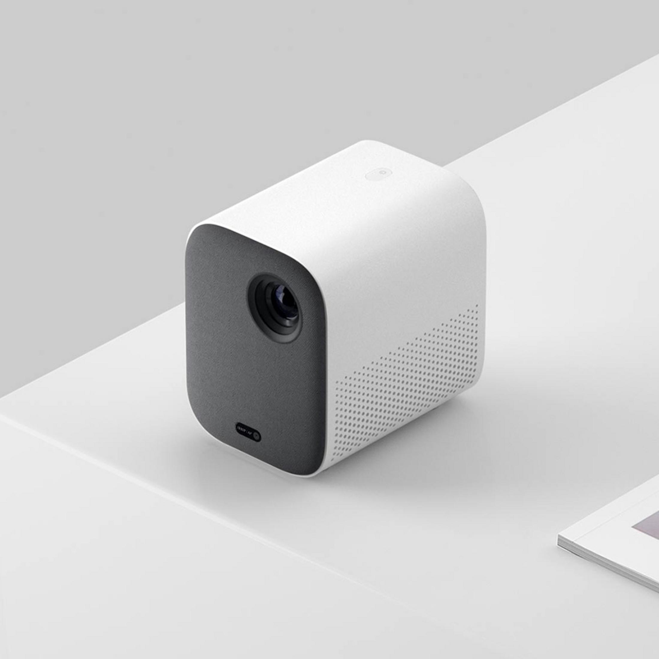 Un proyector cúbico blanco con panel frontal oscuro sobre una superficie blanca.