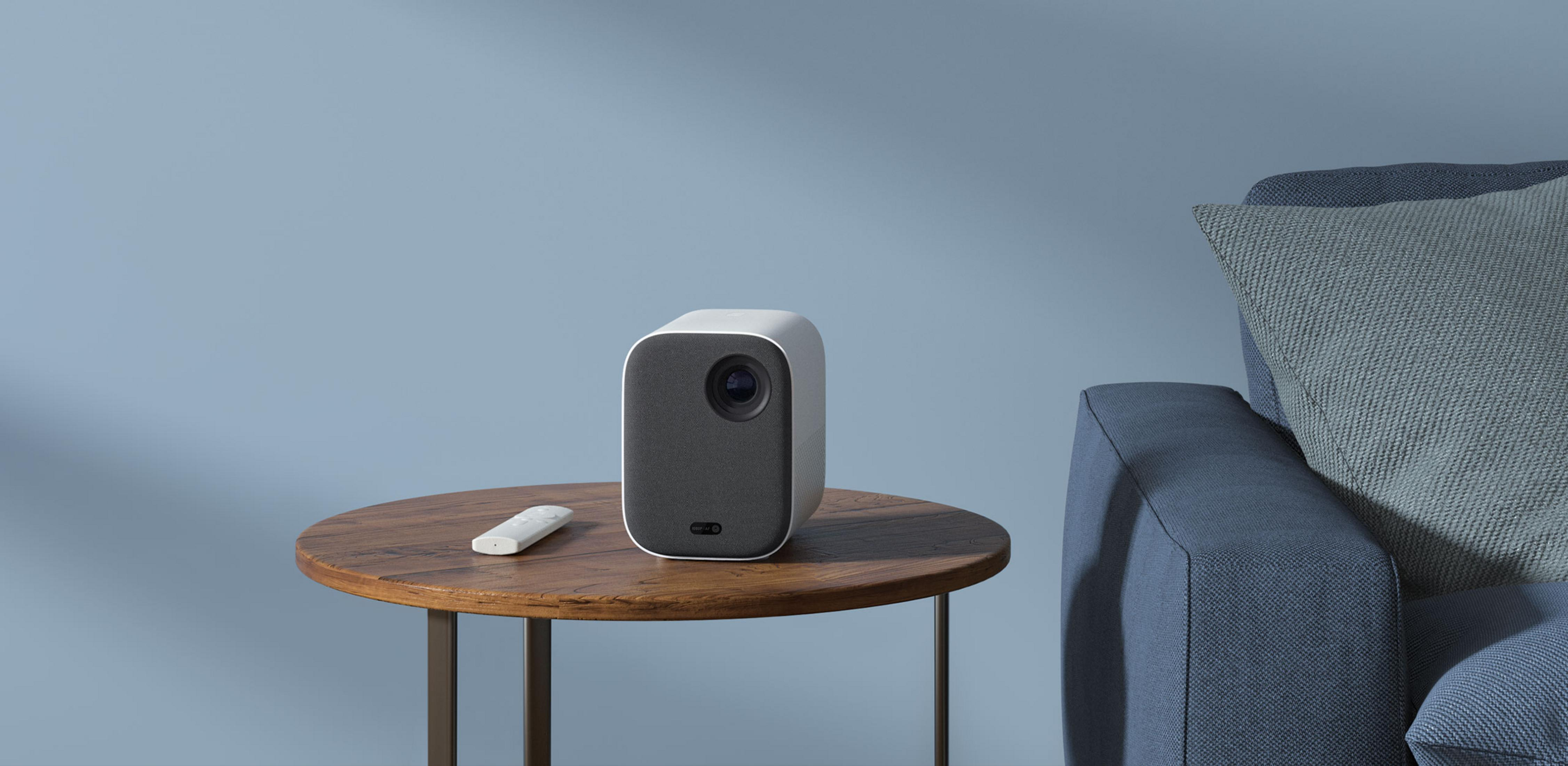 Un proyector blanco con mando a distancia sobre una mesa de madera.