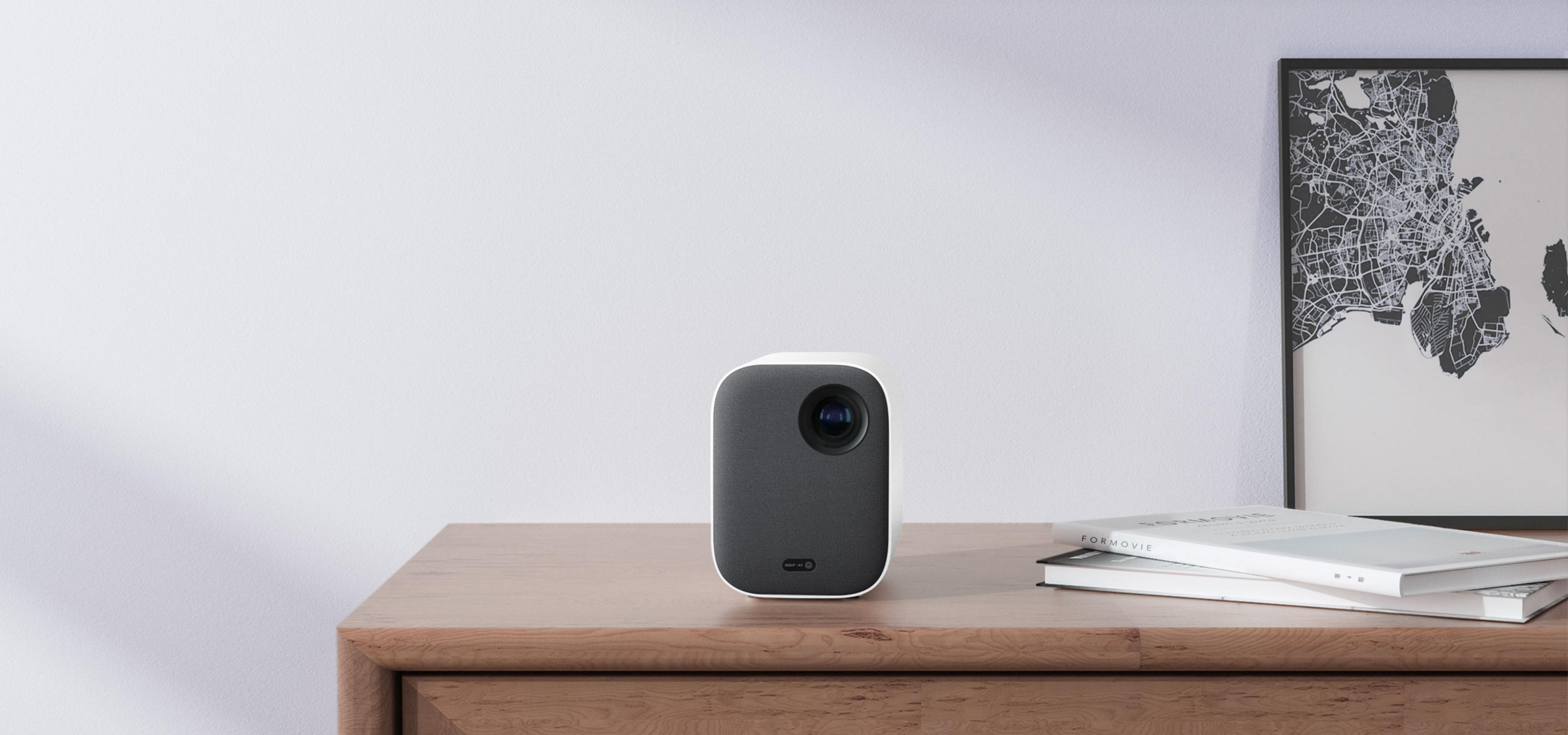 Un proyector compacto se sienta en una mesa de madera junto a dos libros y un mapa.