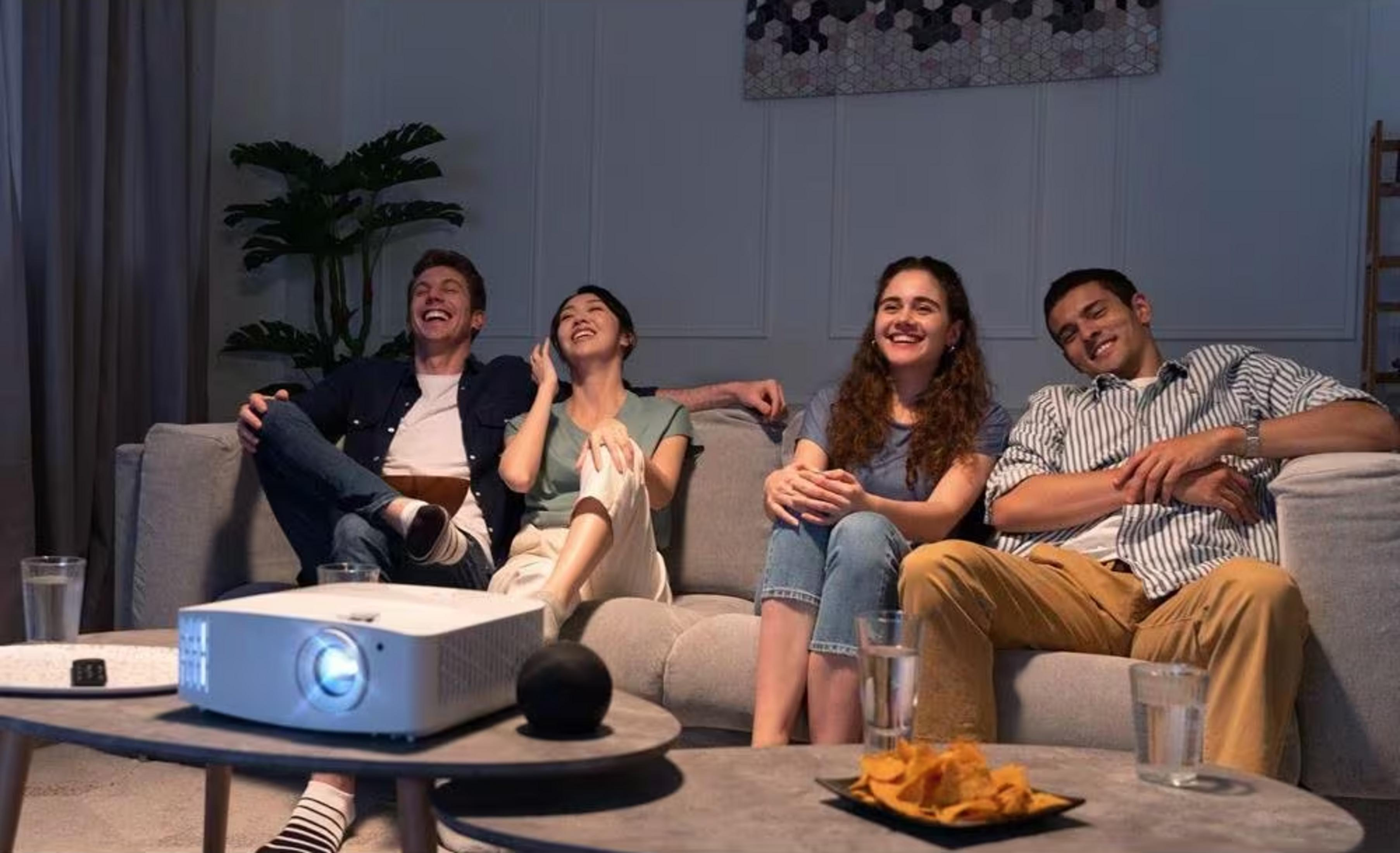 Cuatro amigos riendo ven un proyector en una mesa de centro.