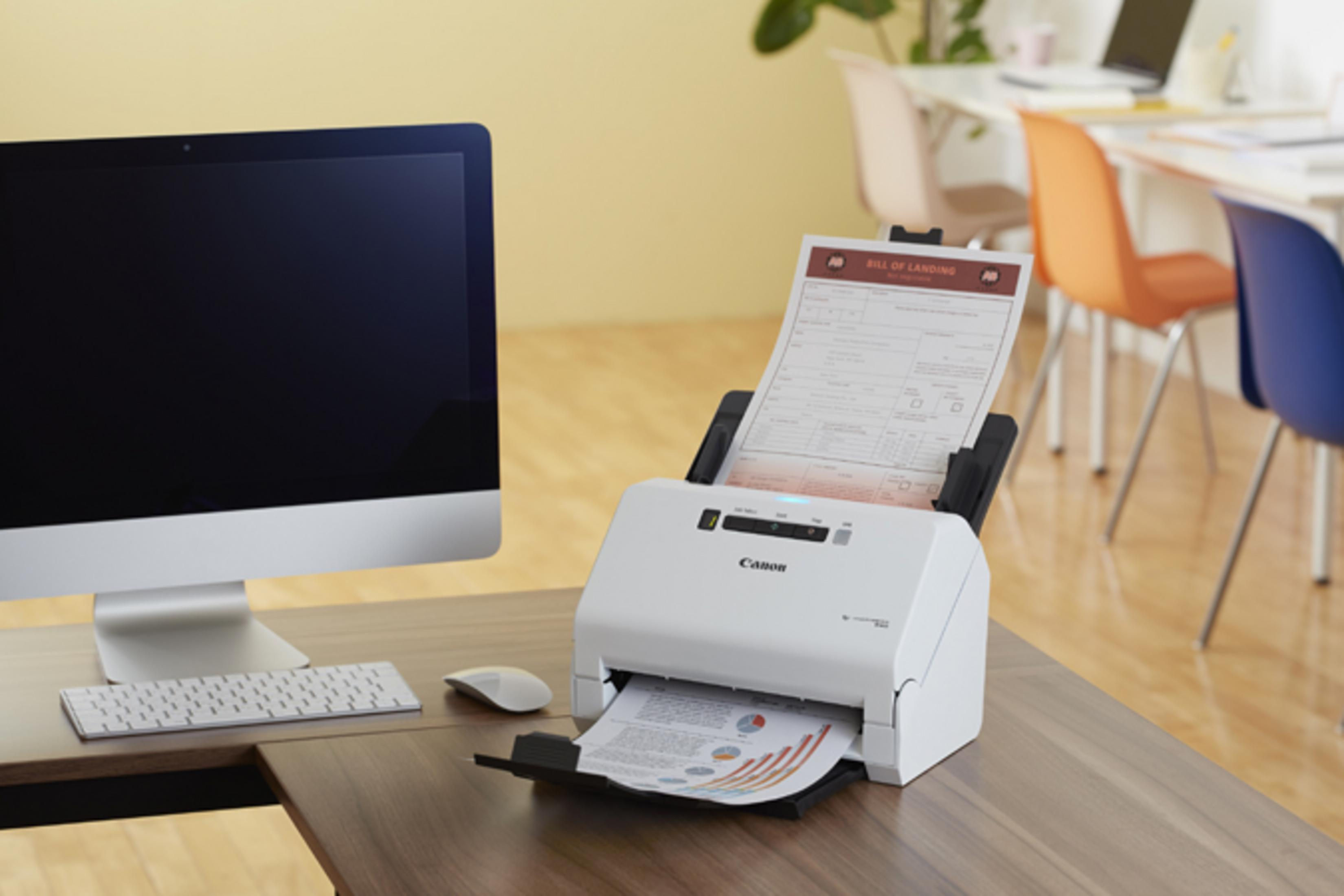 Skaner Canon skanuje dokument z wykresami. Obok monitor i klawiatura.