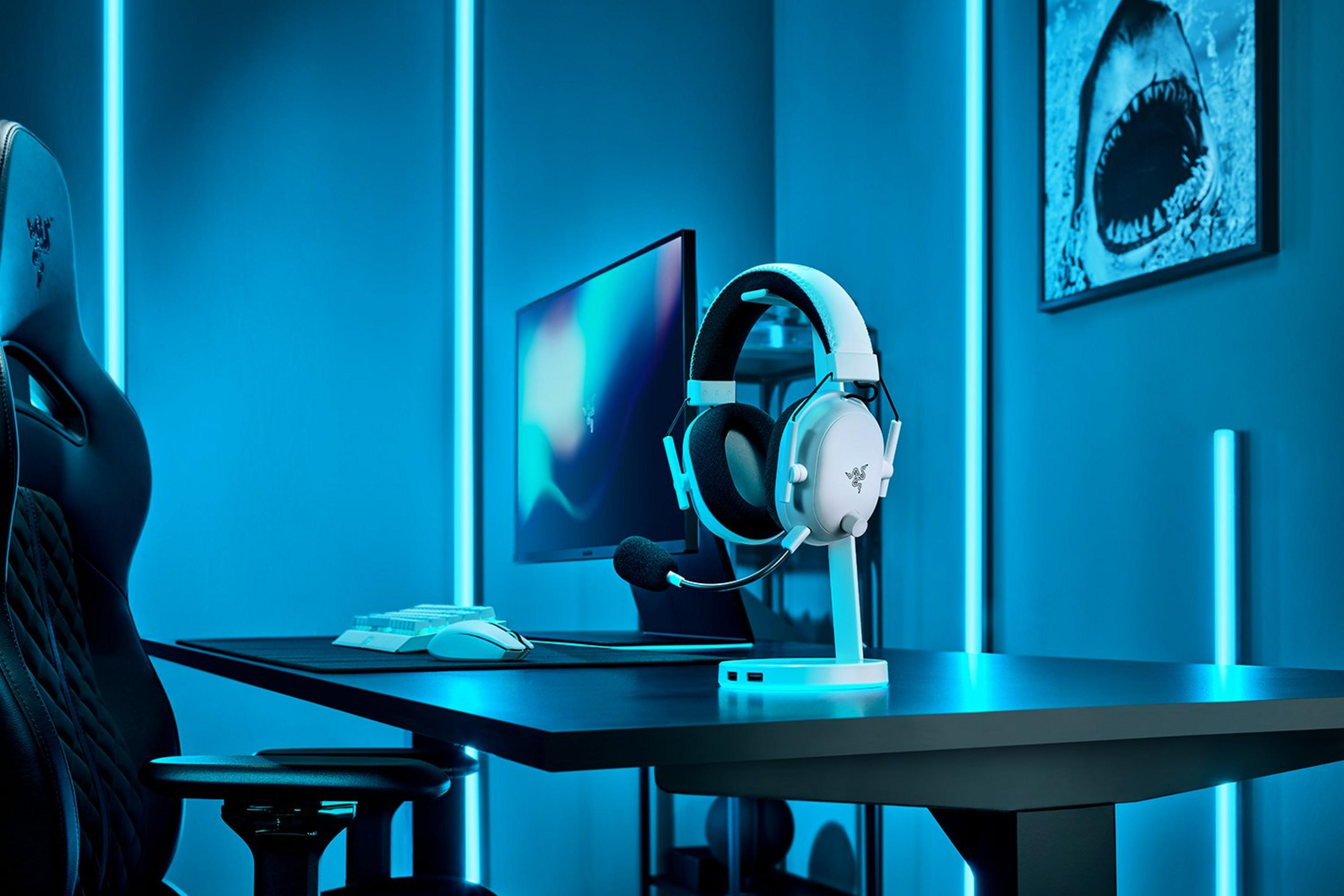Un headset bianco su un supporto di ricarica, vicino a un monitor e un mouse.