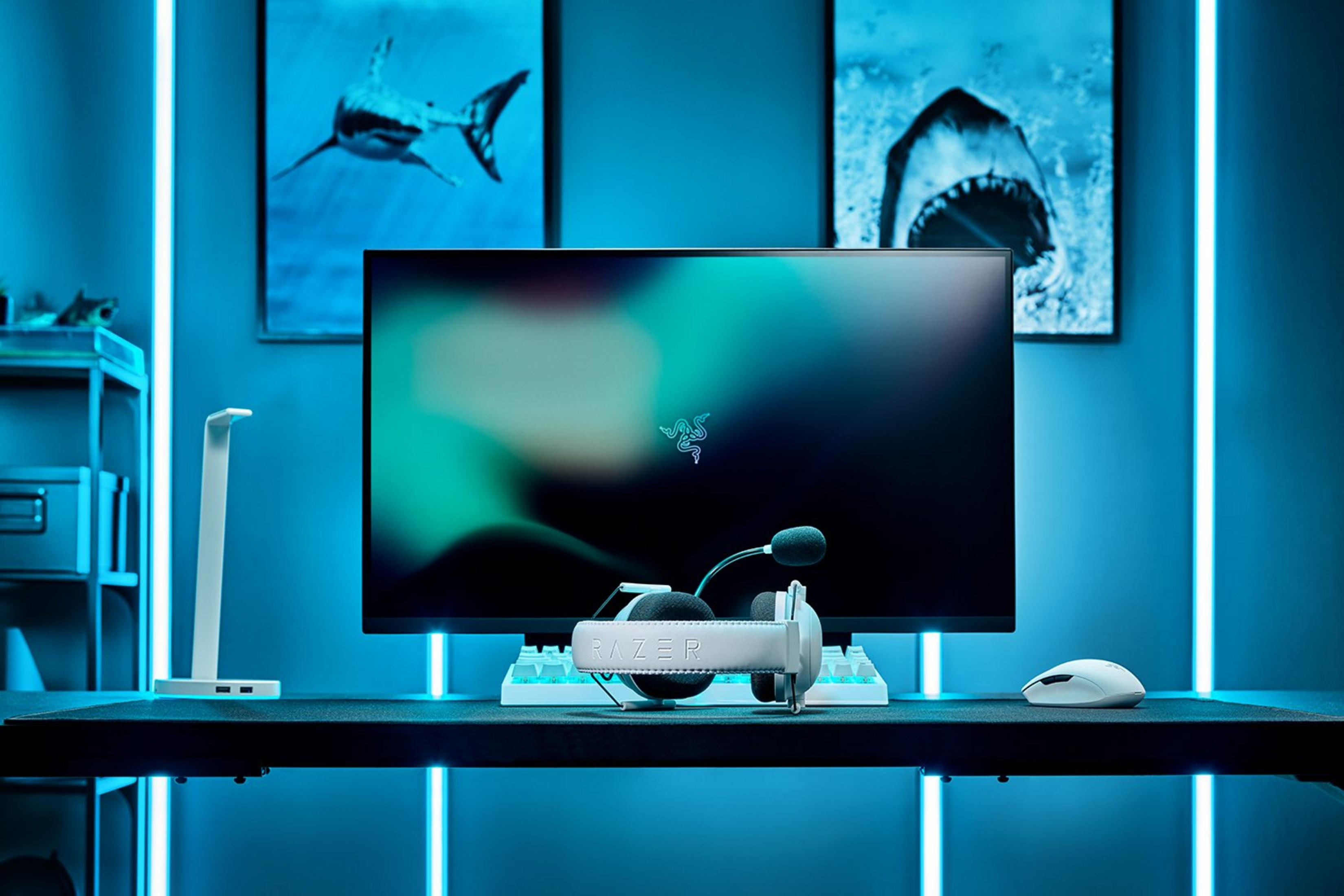 Una scrivania con monitor, tastiera, mouse e cuffie, illuminata da luci al neon blu.