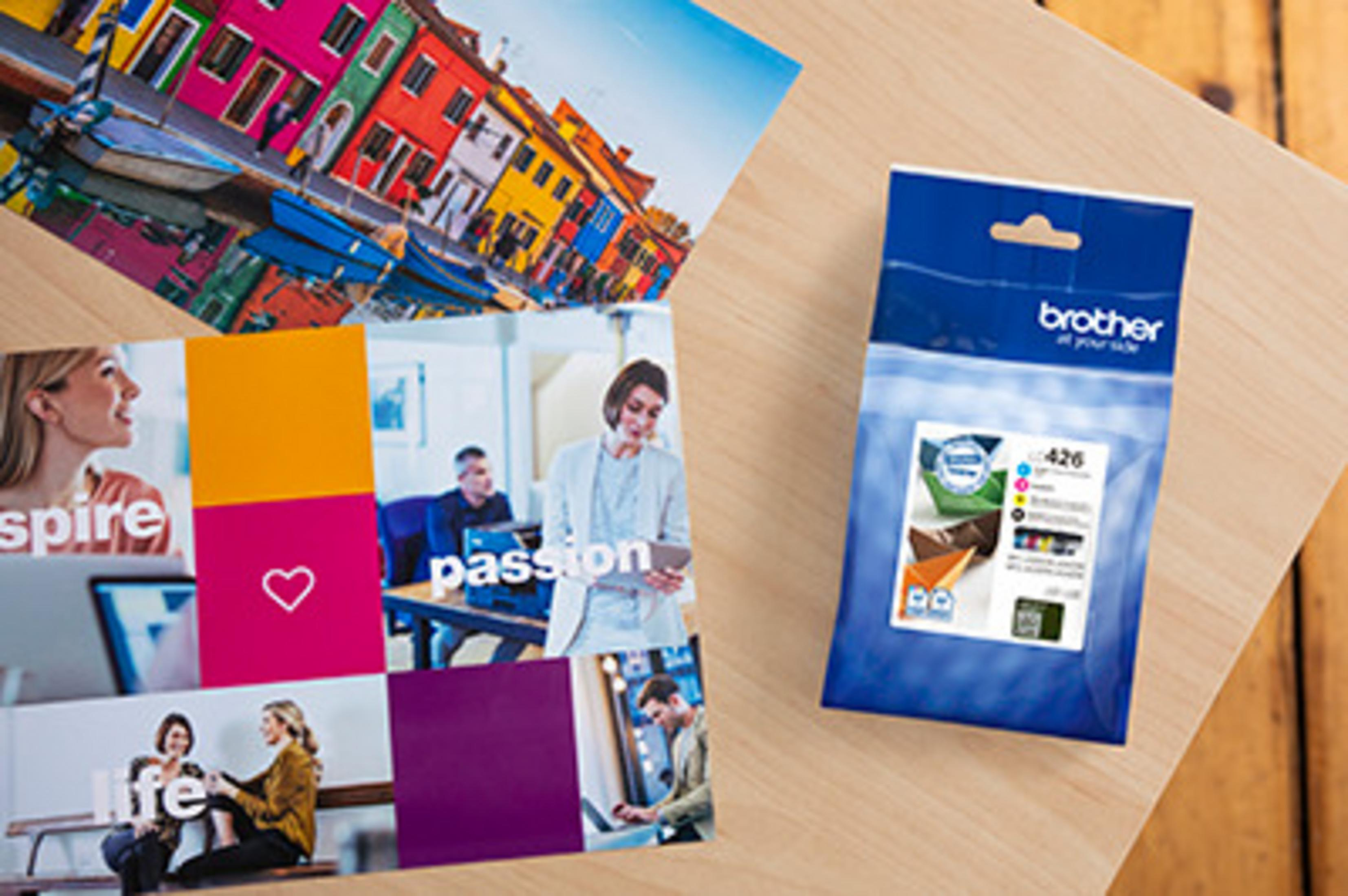 Kolorowe pocztówki i niebieski tusz Brother na drewnianym stole.