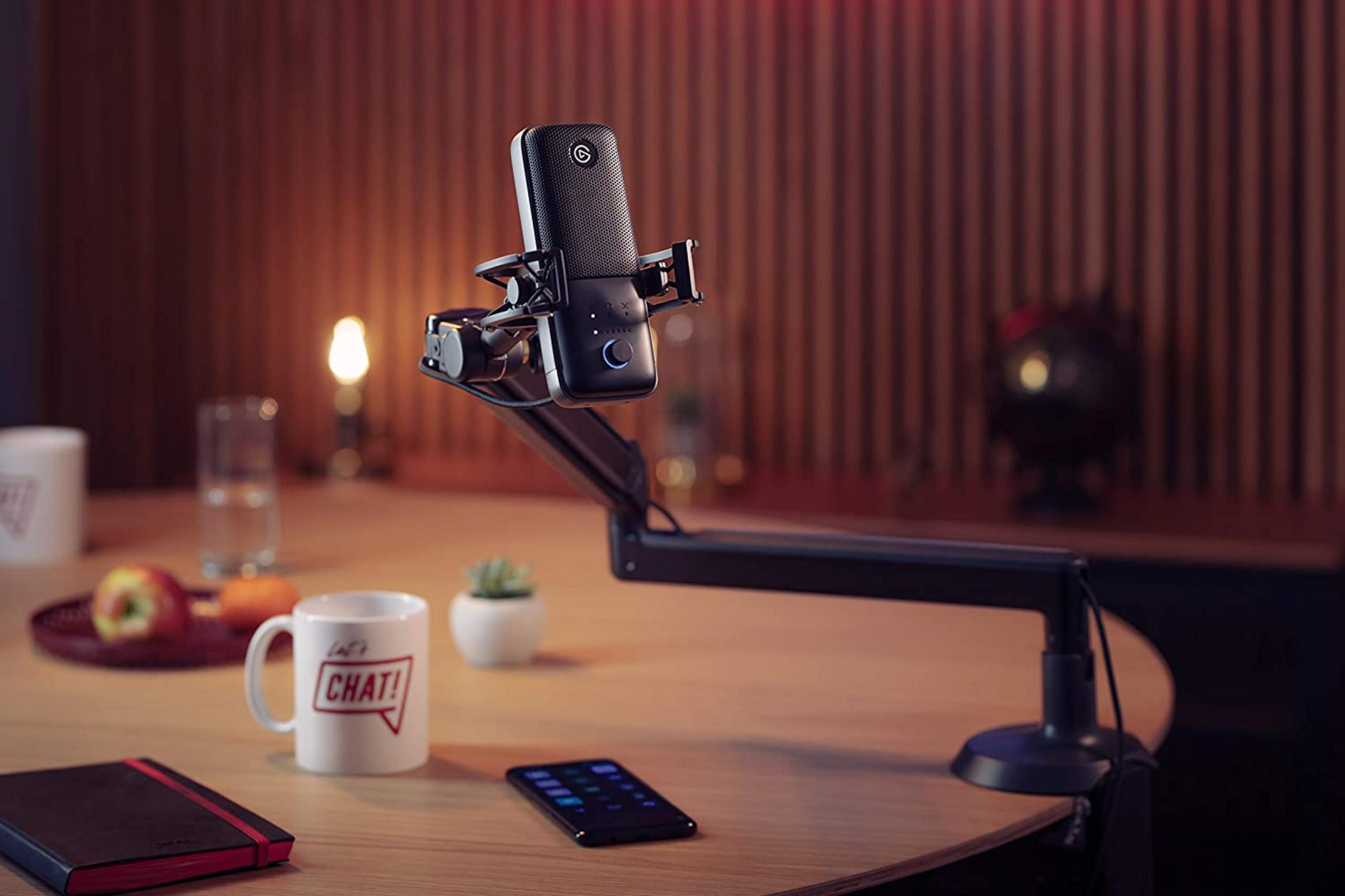 Ein schwarzes Mikrofon auf einem Schreibtisch mit Tasse, Apfel und Notizbuch.